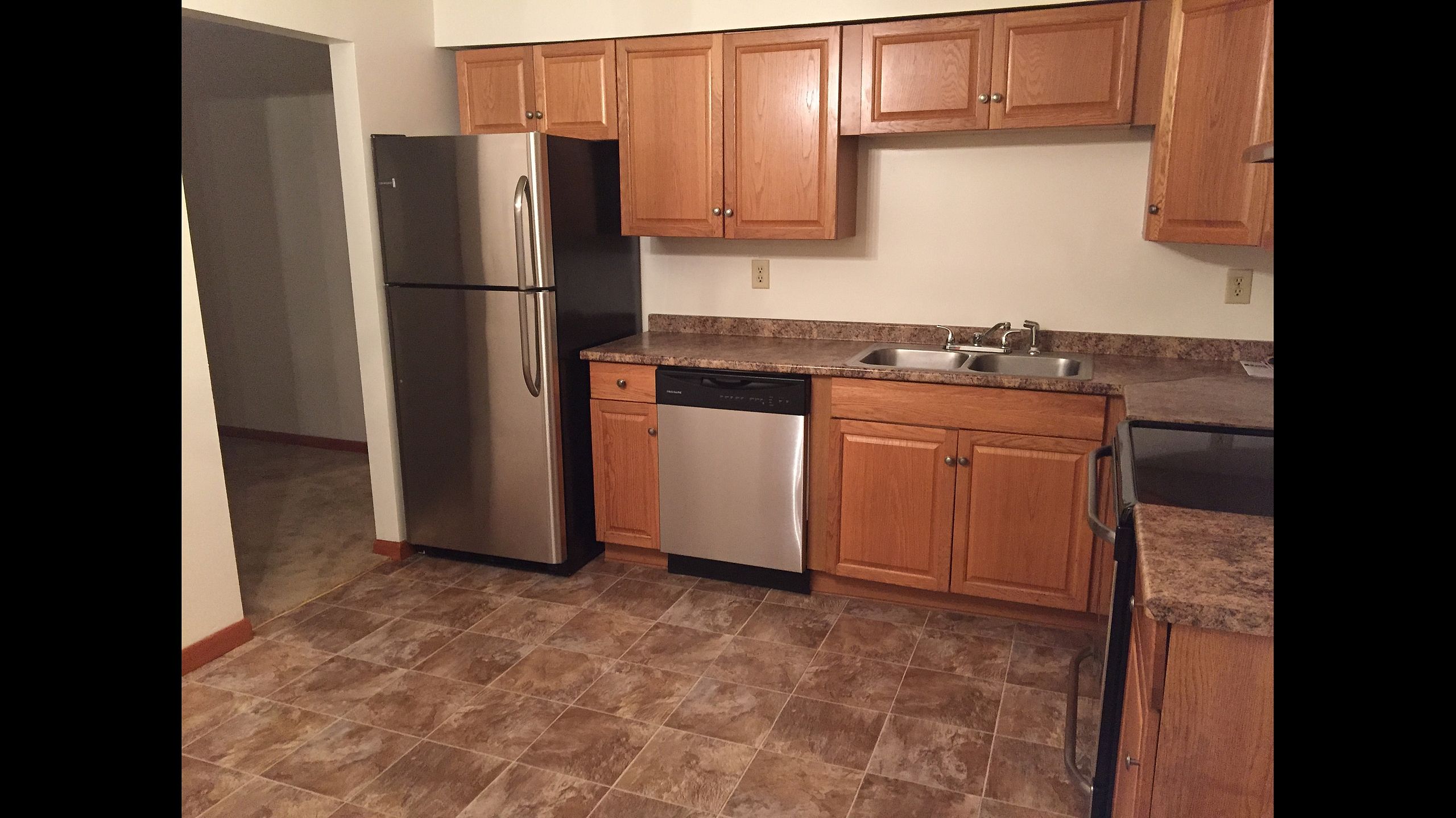 Kitchen with stainless steel refrigerator and dishwasher, wood cabinets and tile floor at Pine Park Terrace Apartments