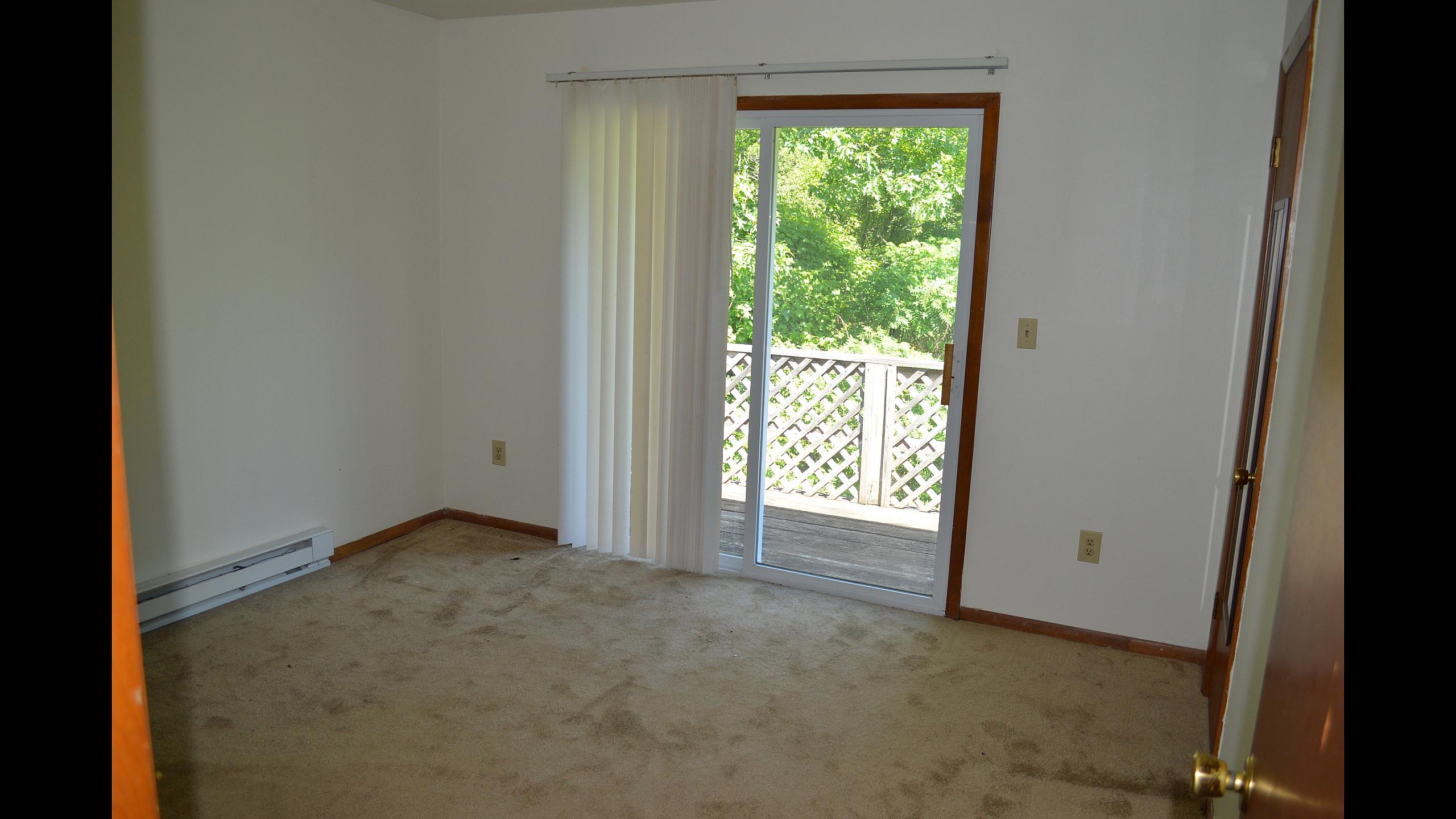Carpeted living area with sliding glass door opening onto a private deck at Pine Park Terrace Apartments