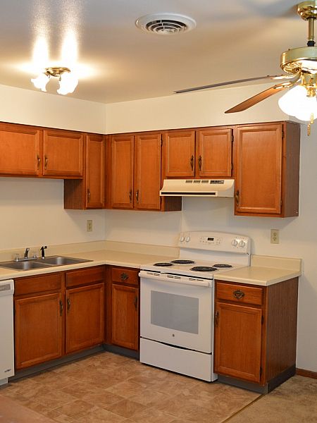 Apartment kitchen with full-size range, wood cabinets and ceiling fan at Pine Park Terrace Apartments