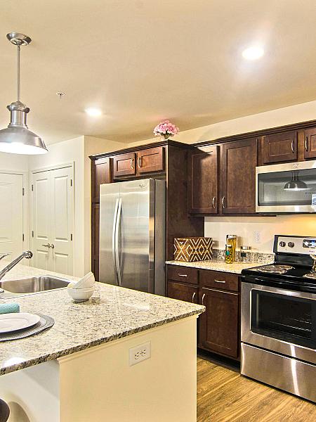 Kitchen with granite island, stainless steel appliances and wood cabinetry at Van Allen Apartments