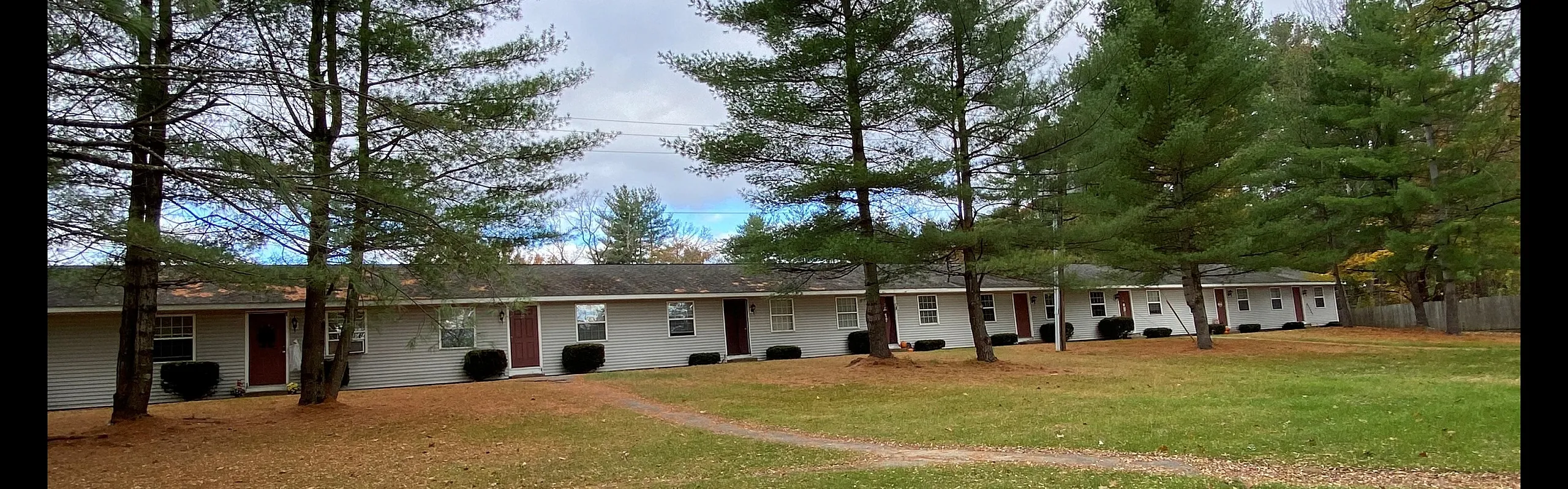 Single-story apartment homes with open lawn and pines at Canfield Apartments in Gansevoort, NY
