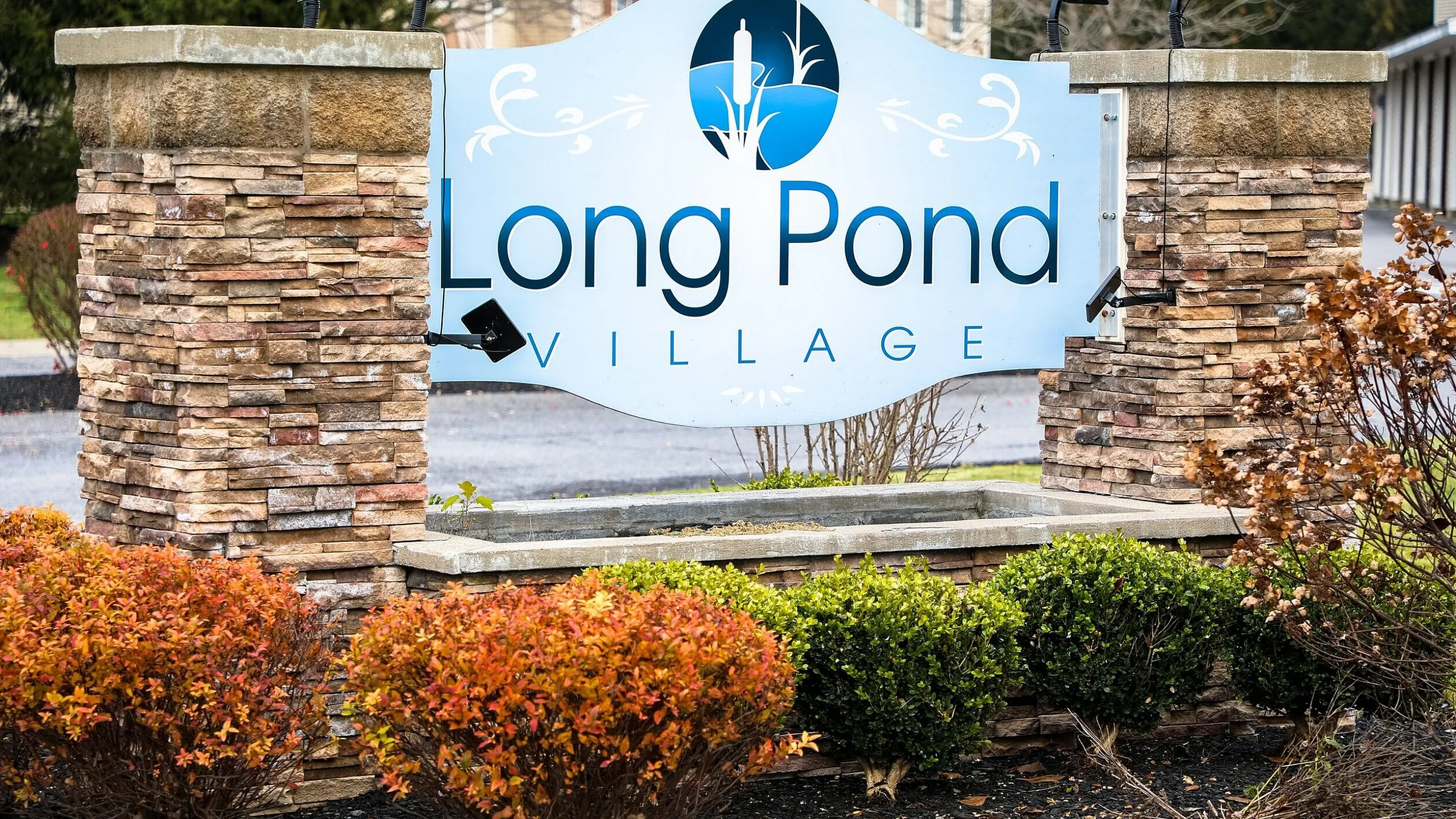 Long Pond Village monument sign with stone wall and seasonal landscaping in Schenectady, NY