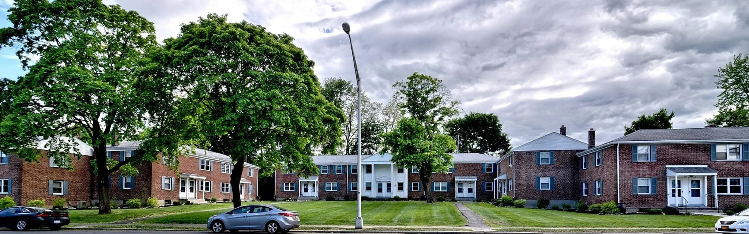 Brick apartment buildings, columned entrance and mature landscaping along the courtyard at Adams Park Apartments in Albany, NY