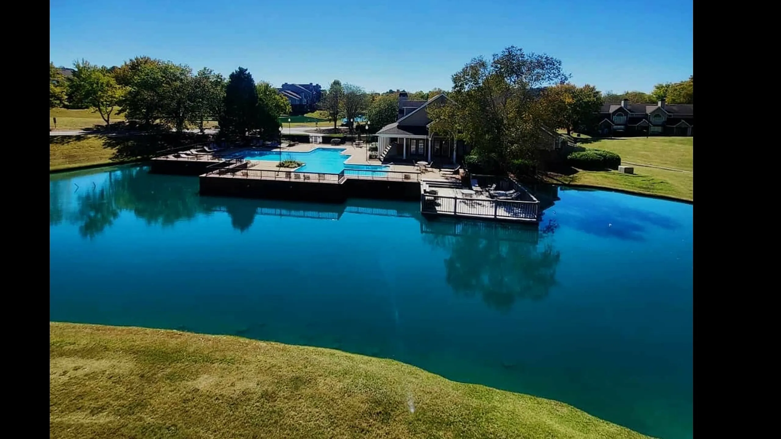 Stunning lakeside view with a sparkling swimming pool, surrounded by lush greenery and clear blue skies.