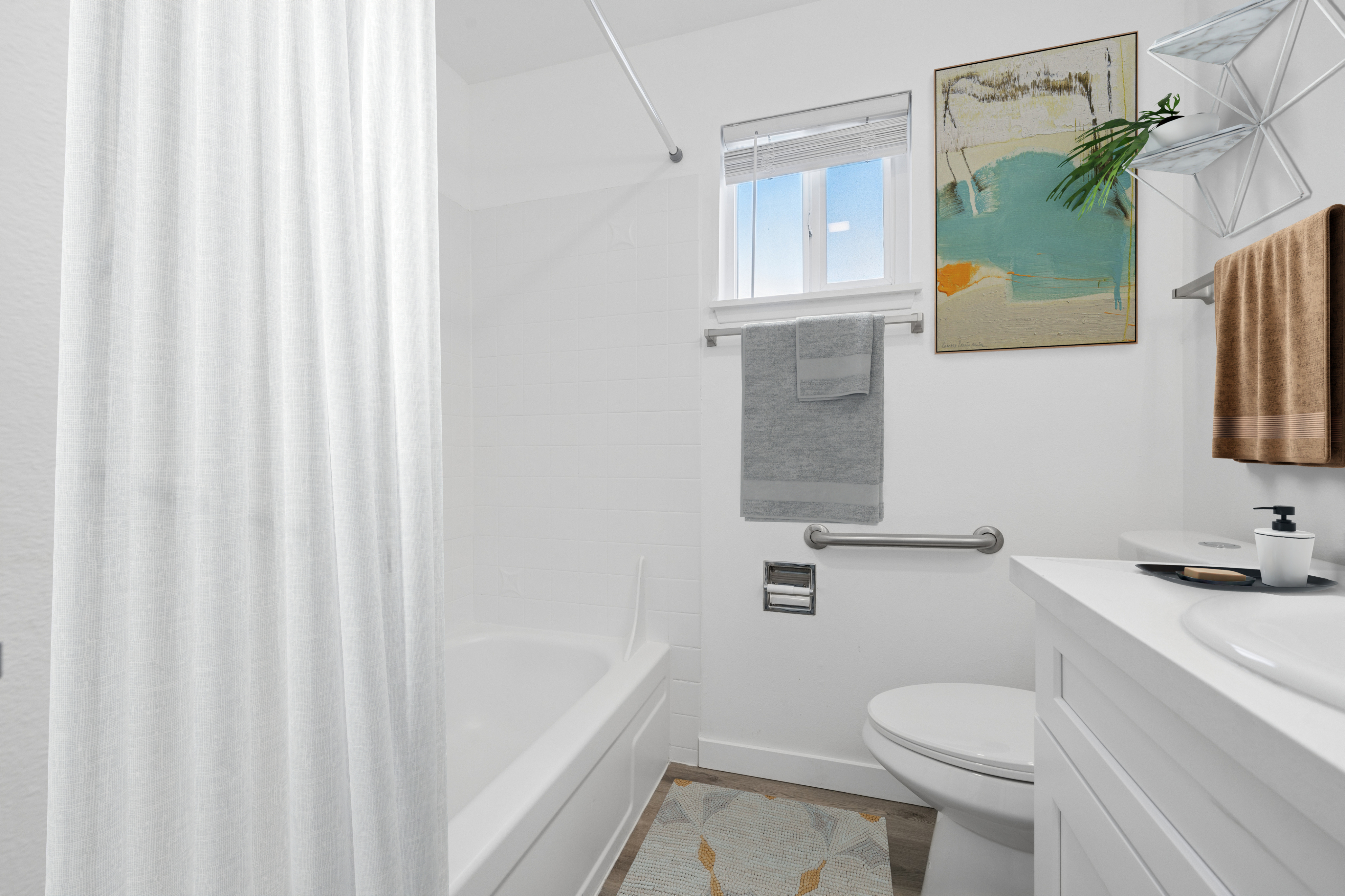 Bright modern bathroom with elegant white accents, stylish artwork, and natural light filtering through a window.