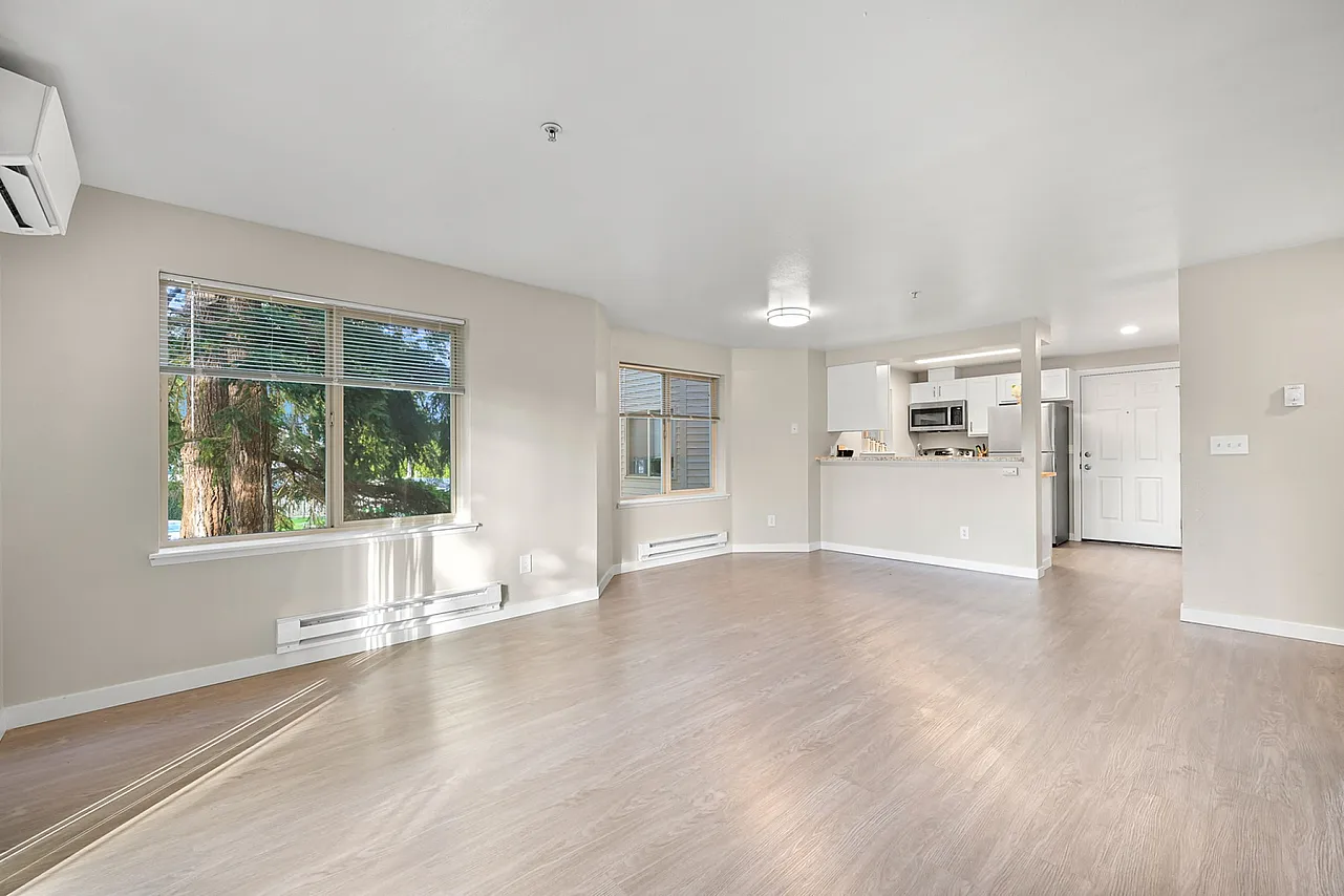 Bright open-concept living area with modern kitchen, large windows, and elegant wood flooring.