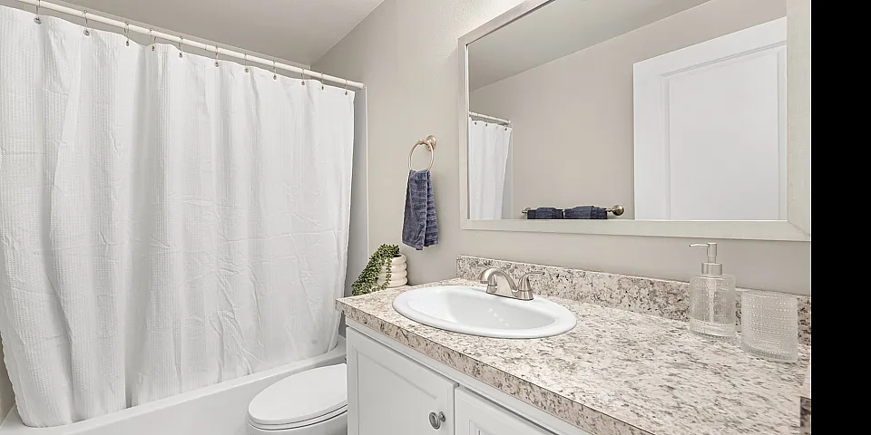 Bright and modern bathroom featuring elegant granite countertops, a large mirror, and a clean white shower curtain, creating a welcoming and pristine atmosphere.