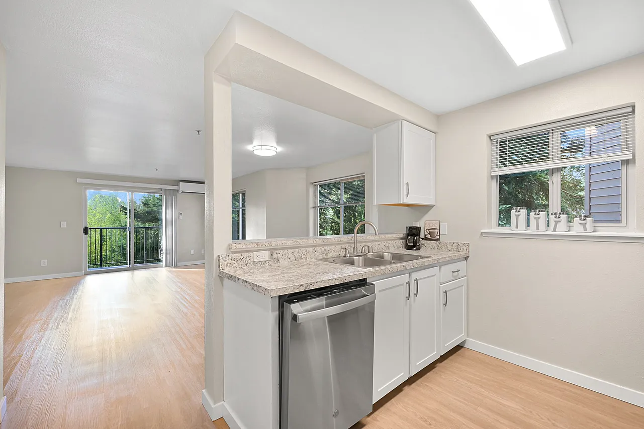 Modern open-concept apartment with a bright kitchen featuring sleek countertops, adjacent to a spacious living area with large windows and balcony access.