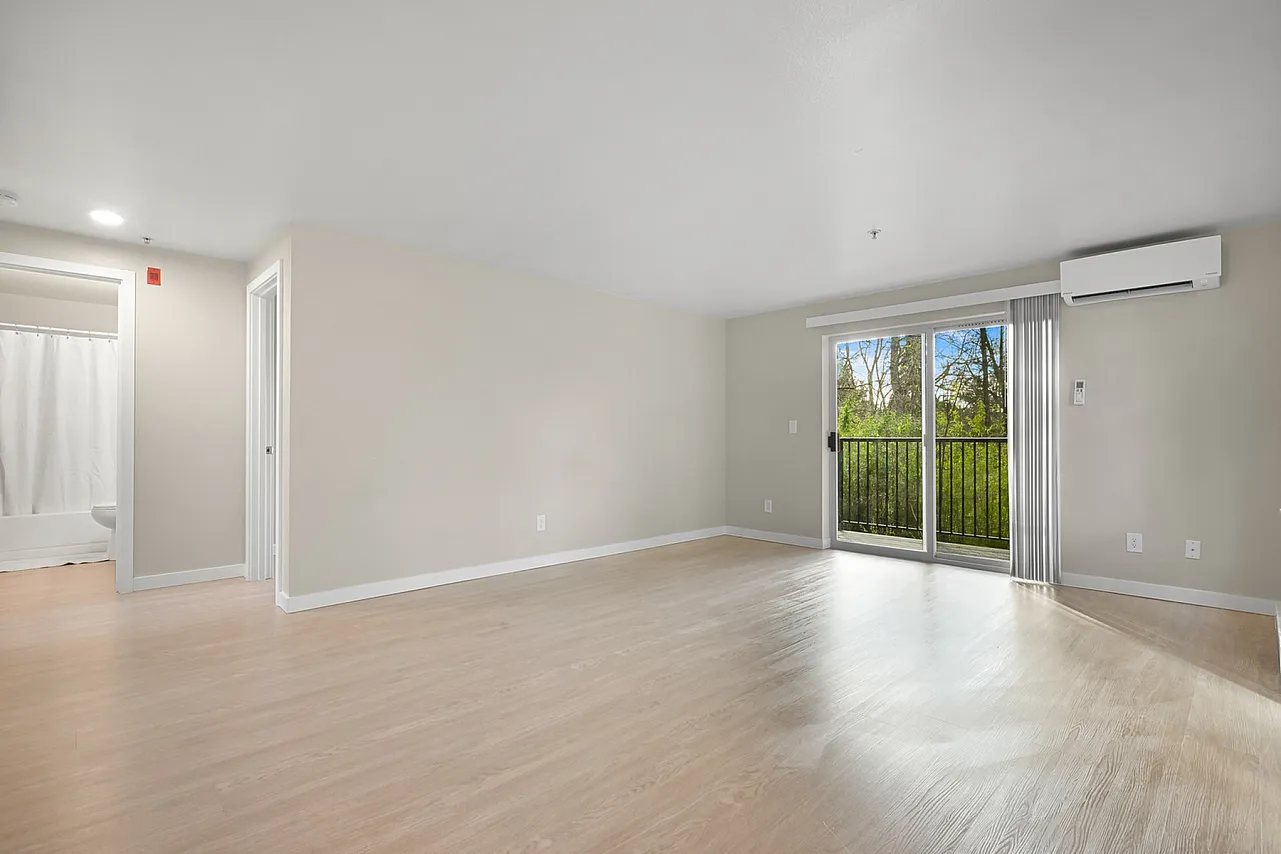 Bright and spacious living area with elegant wooden flooring and large sliding glass doors opening to a serene balcony view.