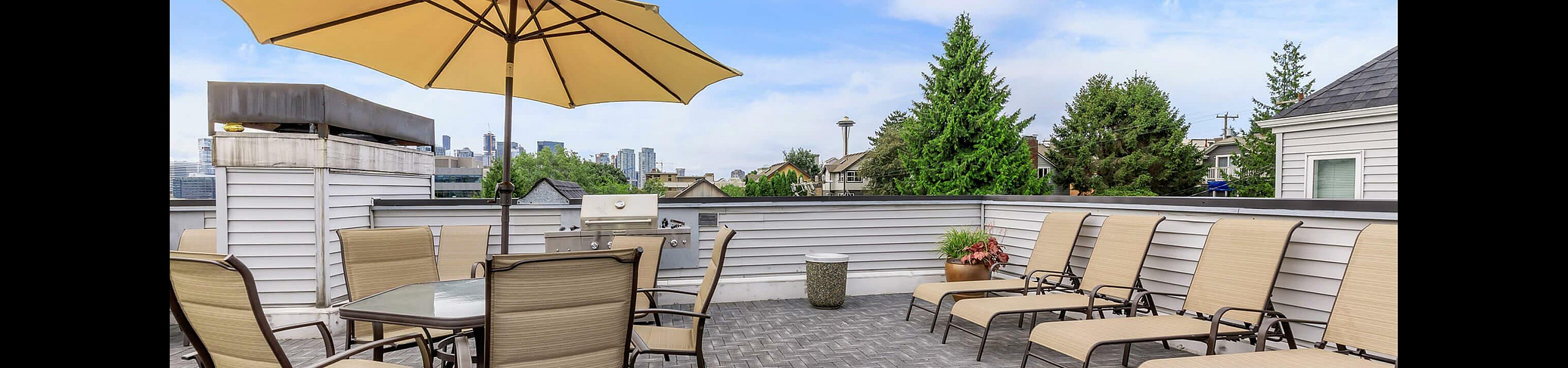 Elegant rooftop patio with modern lounge chairs, a spacious dining area under a stylish umbrella, and a view of the city skyline, perfect for relaxing and entertaining.