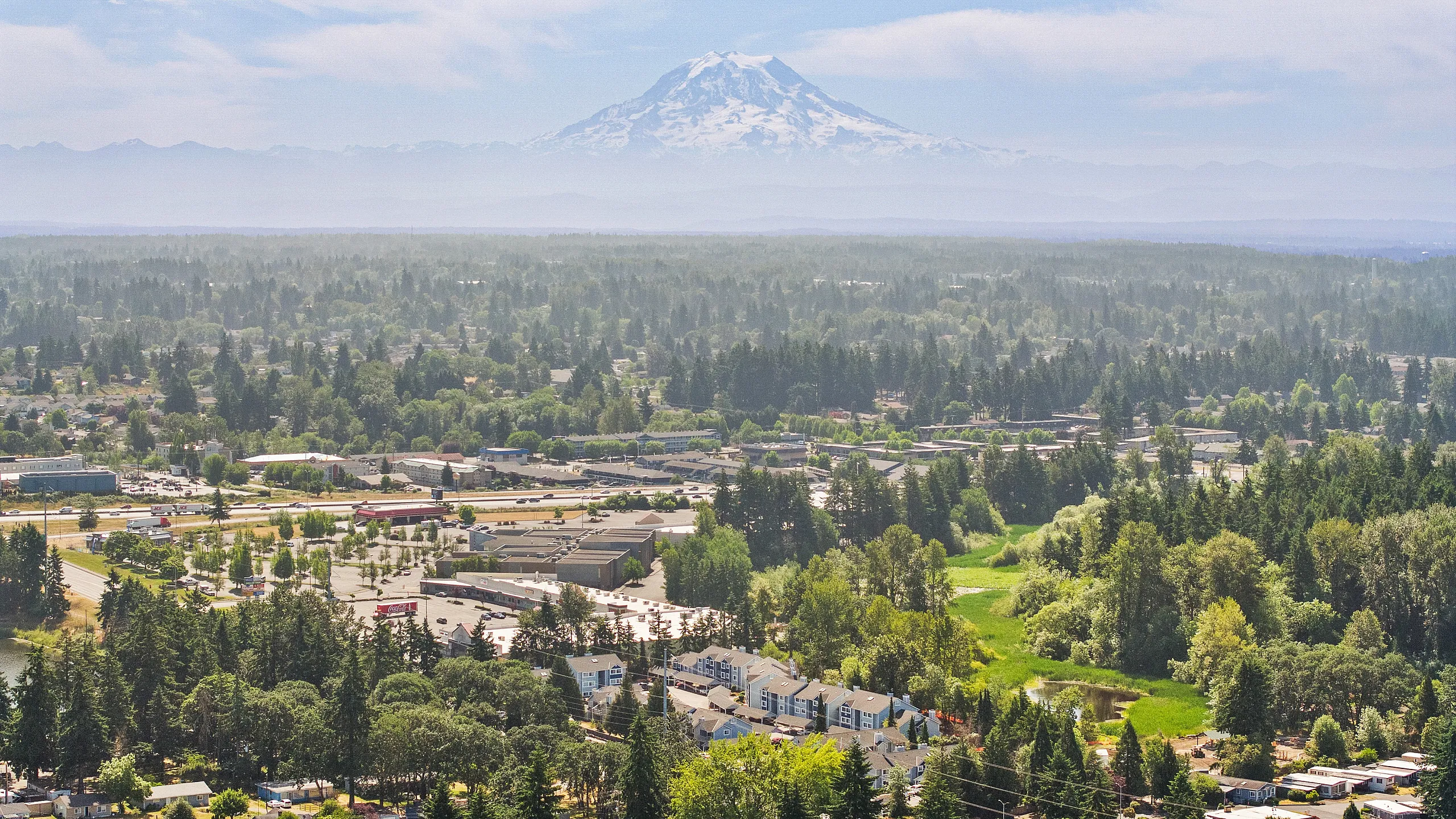 Breathtaking aerial view of lush greenery and a vibrant residential community with a majestic snow-capped mountain in the background.