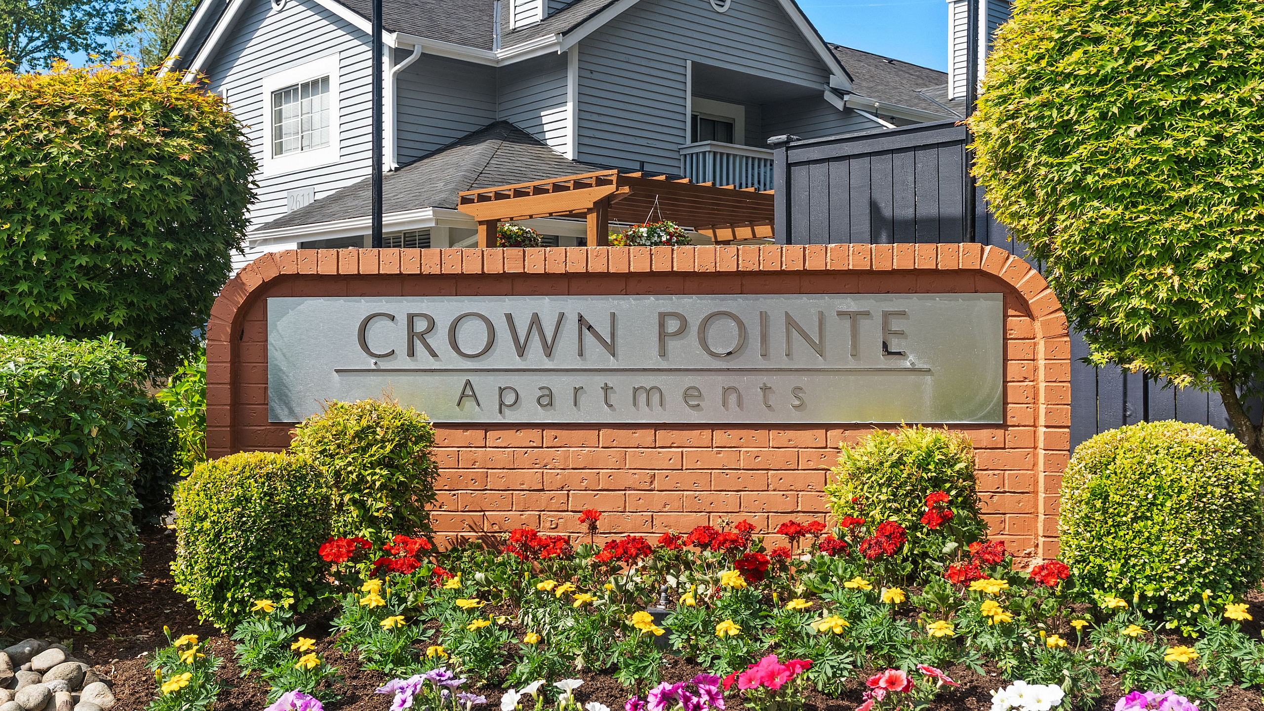 Crown Pointe Apartments entrance with vibrant flower garden and lush greenery, offering a welcoming and serene environment.