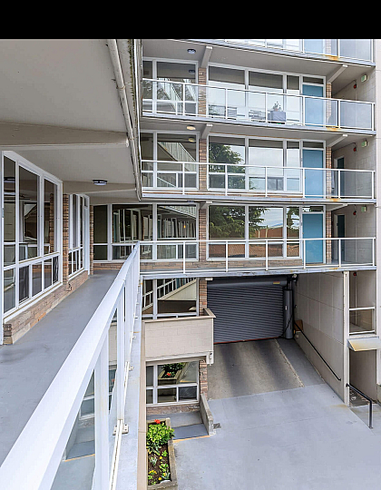 Modern apartment building with glass balconies, large windows, and a sleek entrance, surrounded by a clean, well-maintained courtyard.