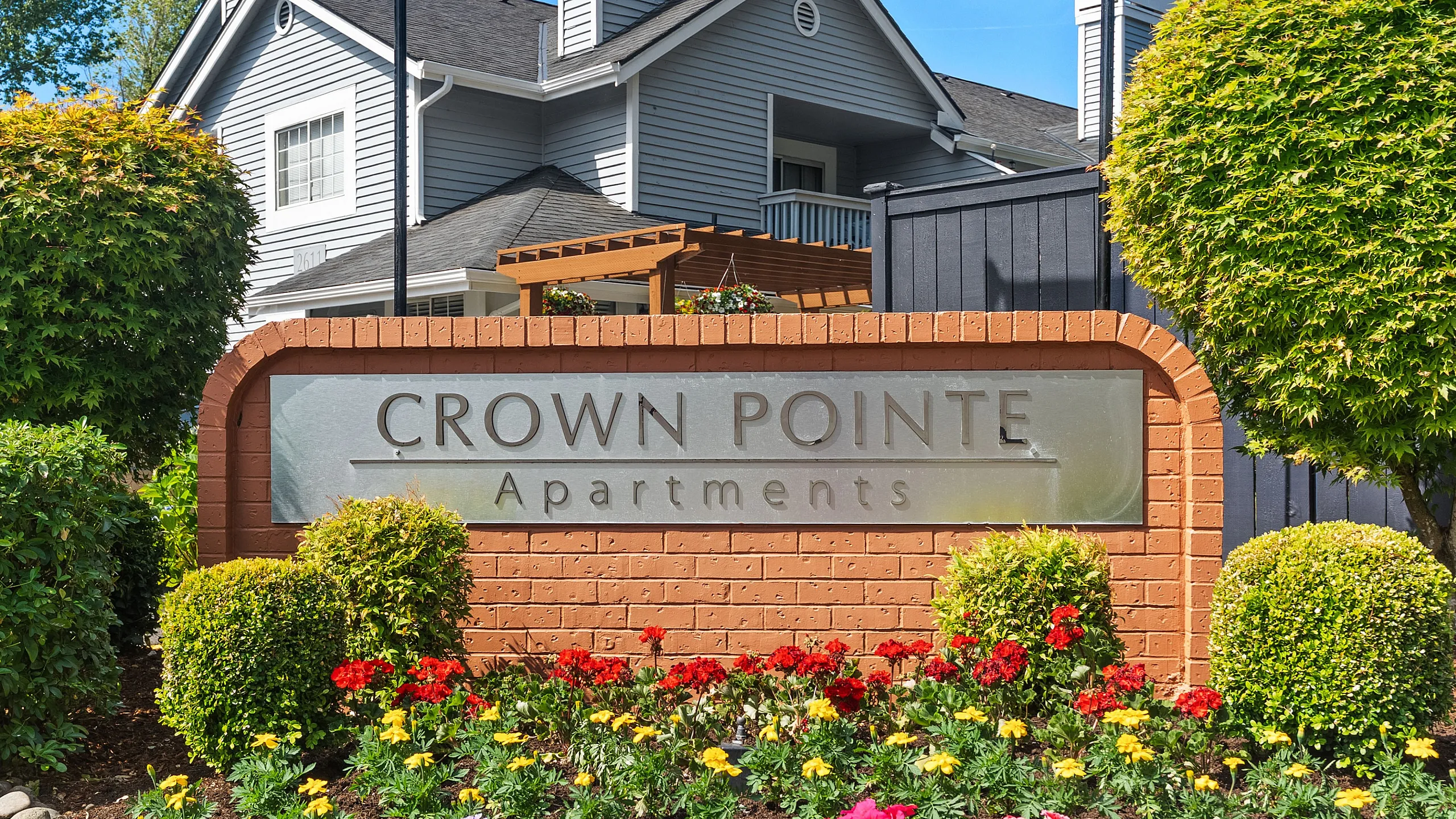 Welcoming Crown Pointe Apartments sign surrounded by vibrant flowers and lush greenery, showcasing inviting architecture in a serene setting.