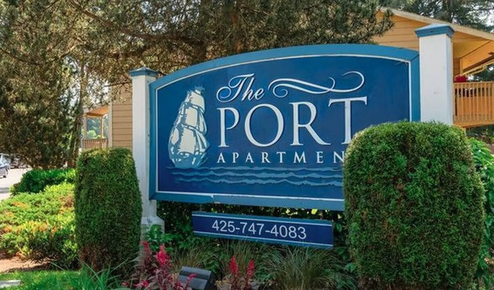 Charming entrance to The Port Apartment, surrounded by lush greenery and tall trees, exuding a warm welcome.