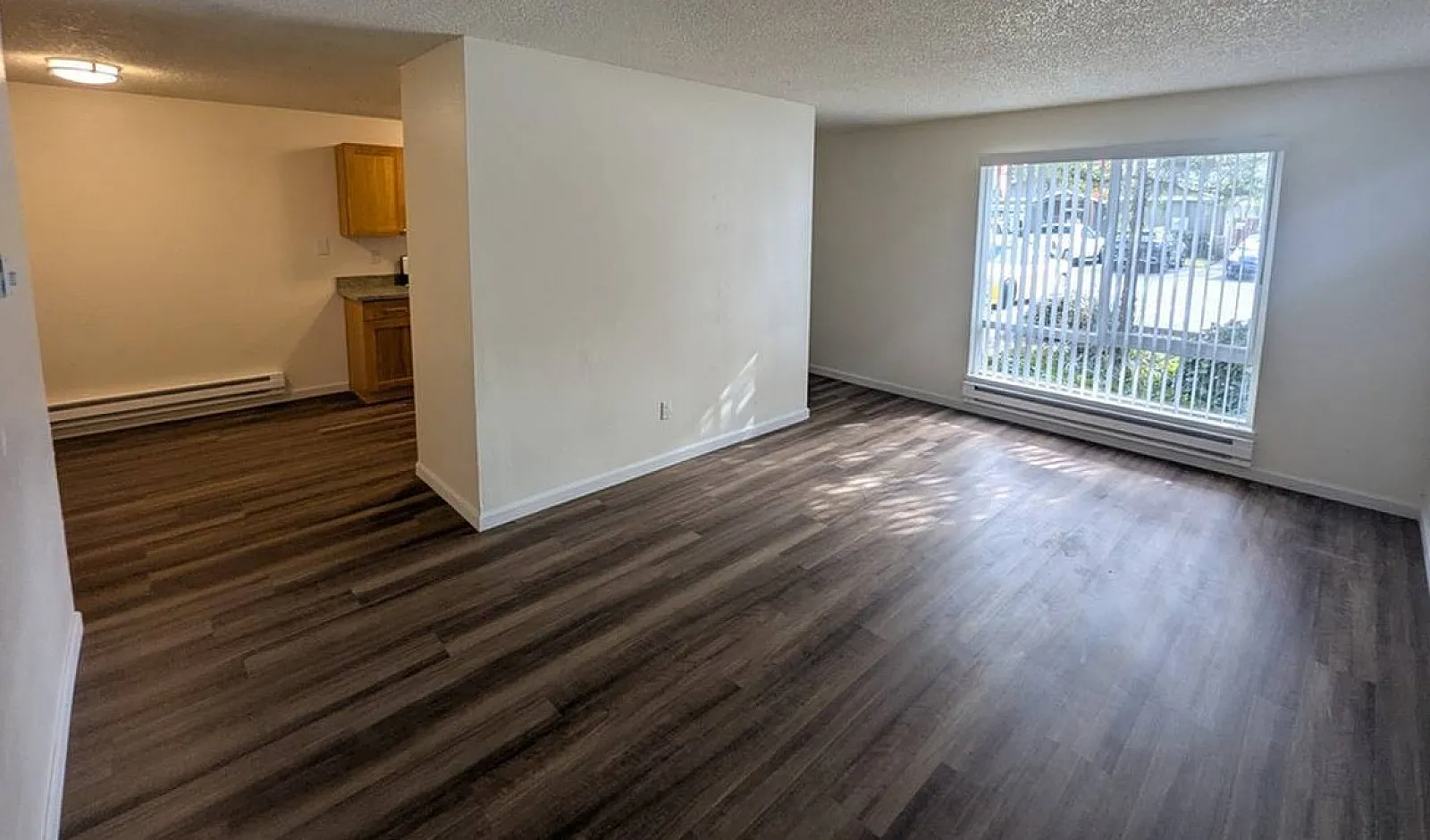 Bright and inviting living area with large window, featuring sleek wood flooring and a cozy kitchen nook.