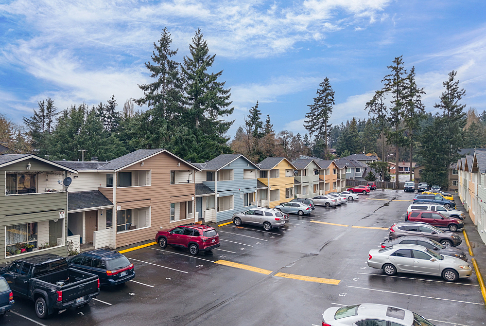 Inviting apartment complex surrounded by lush trees with ample parking space, set under a beautiful blue sky.