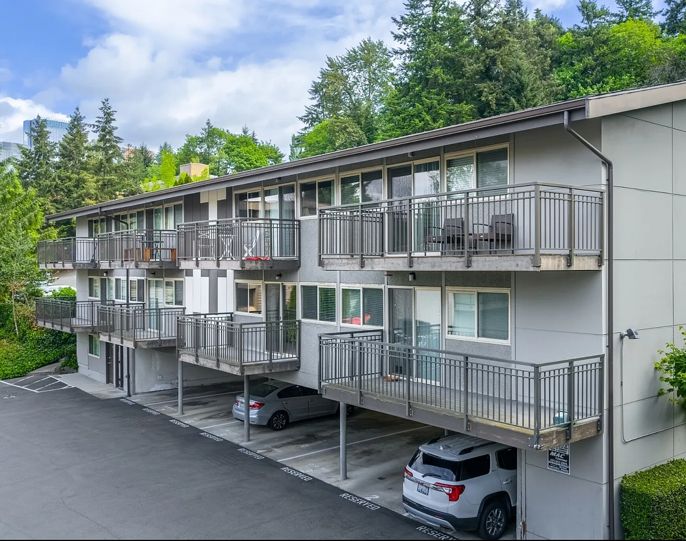 Elegant multi-story apartment complex surrounded by lush greenery, featuring spacious private balconies and convenient covered parking.