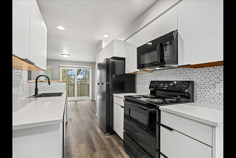 Sleek modern kitchen with black appliances, white cabinetry, and geometric backsplash, accentuated by natural light from large sliding doors.