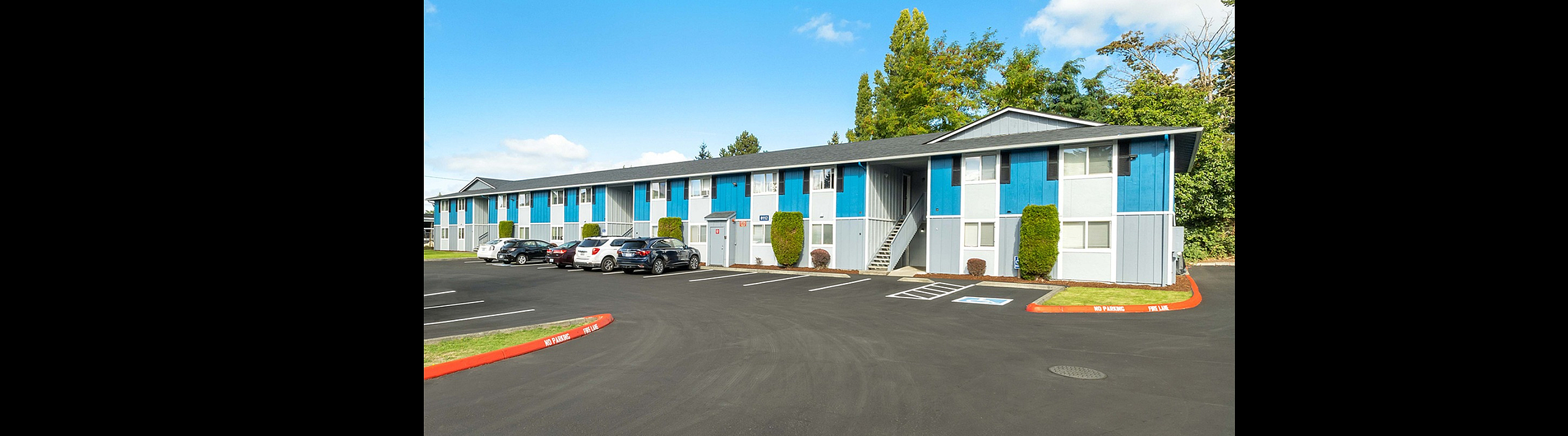 Contemporary apartment building with vibrant blue accents, ample parking, and lush greenery in a serene neighborhood.
