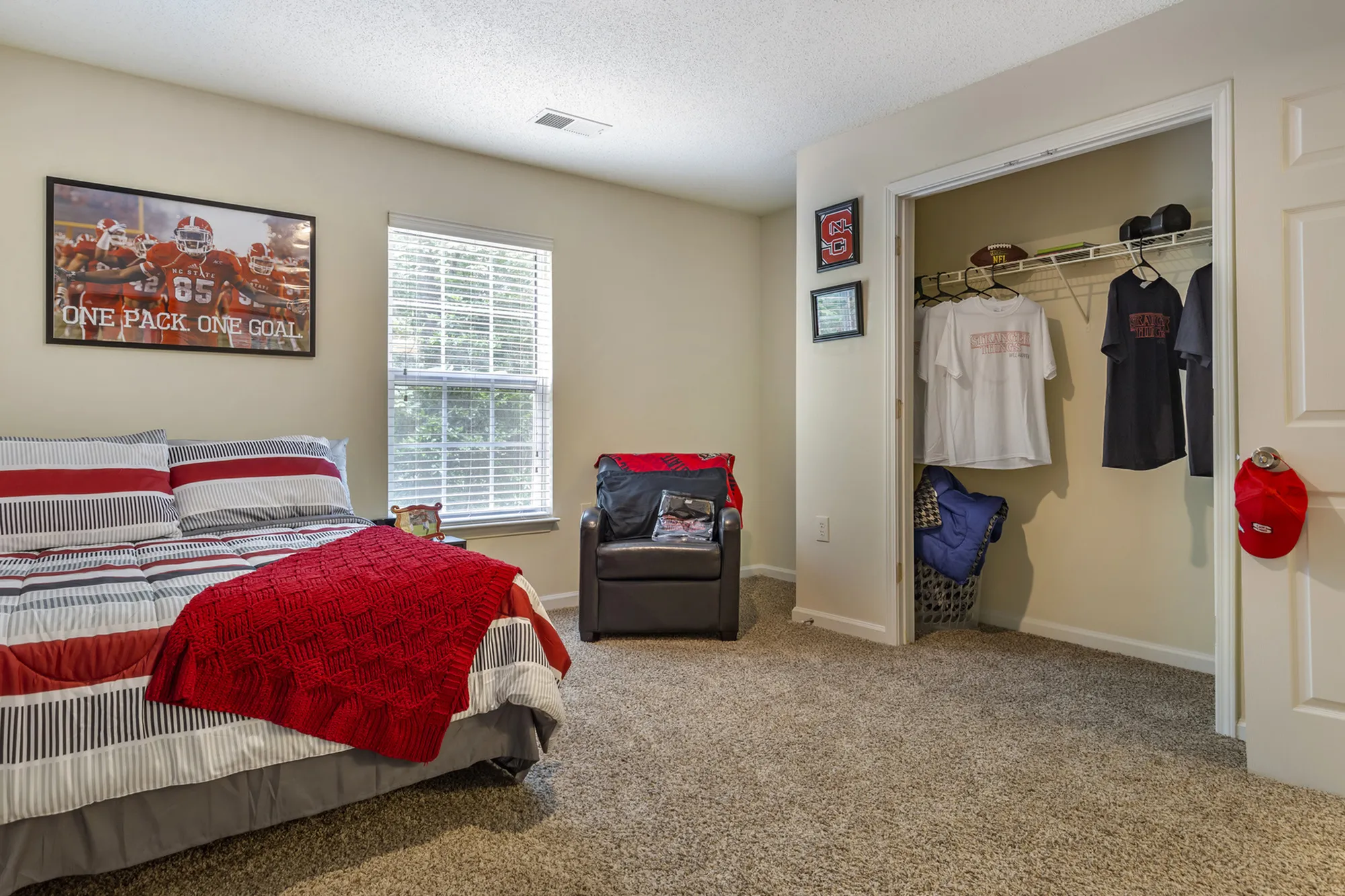 Inviting bedroom featuring a comfortable bed with striped bedding, a cozy armchair, and an open closet with hanging clothes.