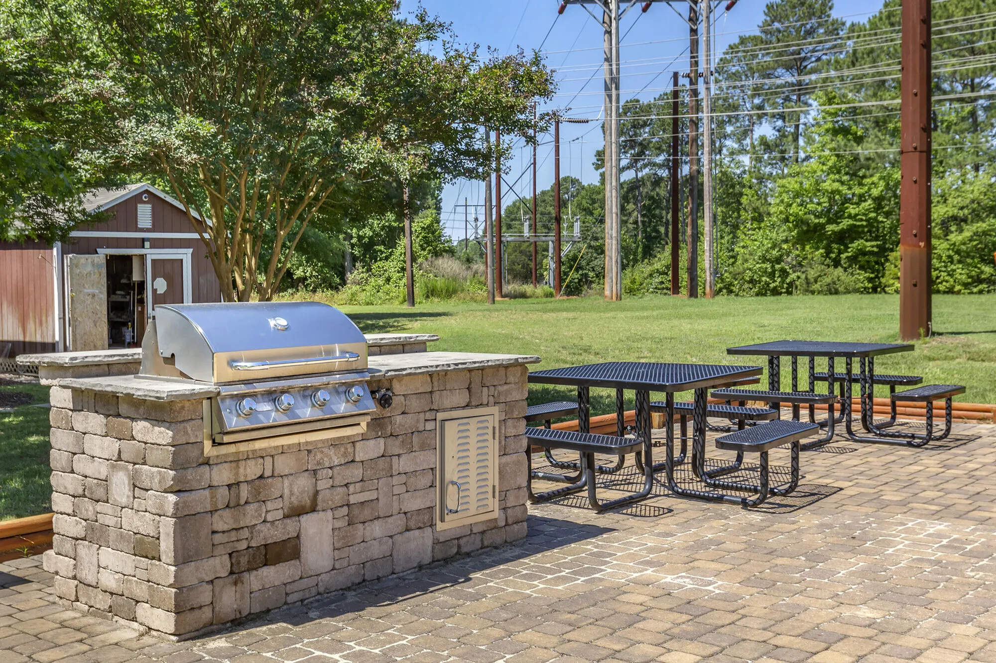 Inviting outdoor grilling station with stainless steel grill and picnic tables in a lush green setting.