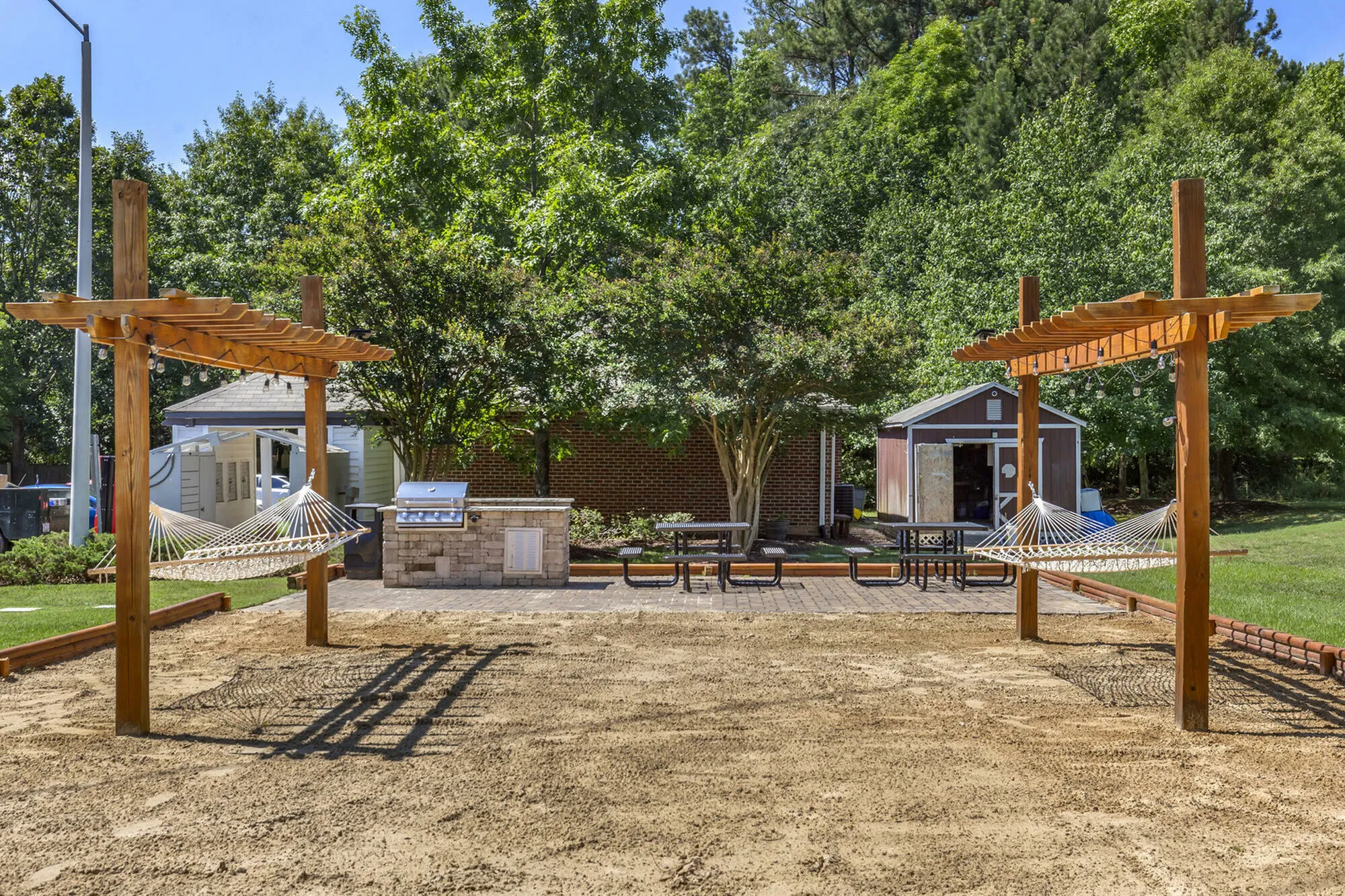 Charming outdoor area with wooden pergolas, hammocks, and barbecue setup surrounded by lush greenery.