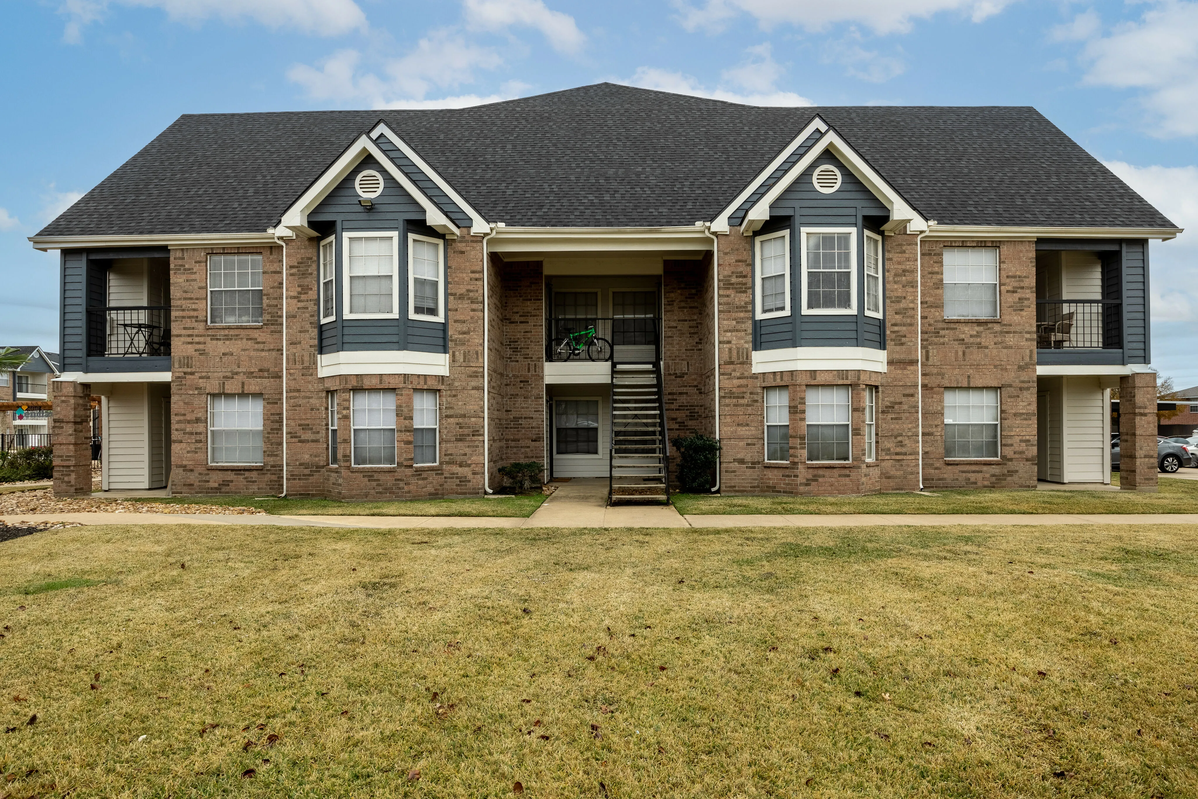 Quaint two-story brick apartment building with bay windows and well-maintained lawn.