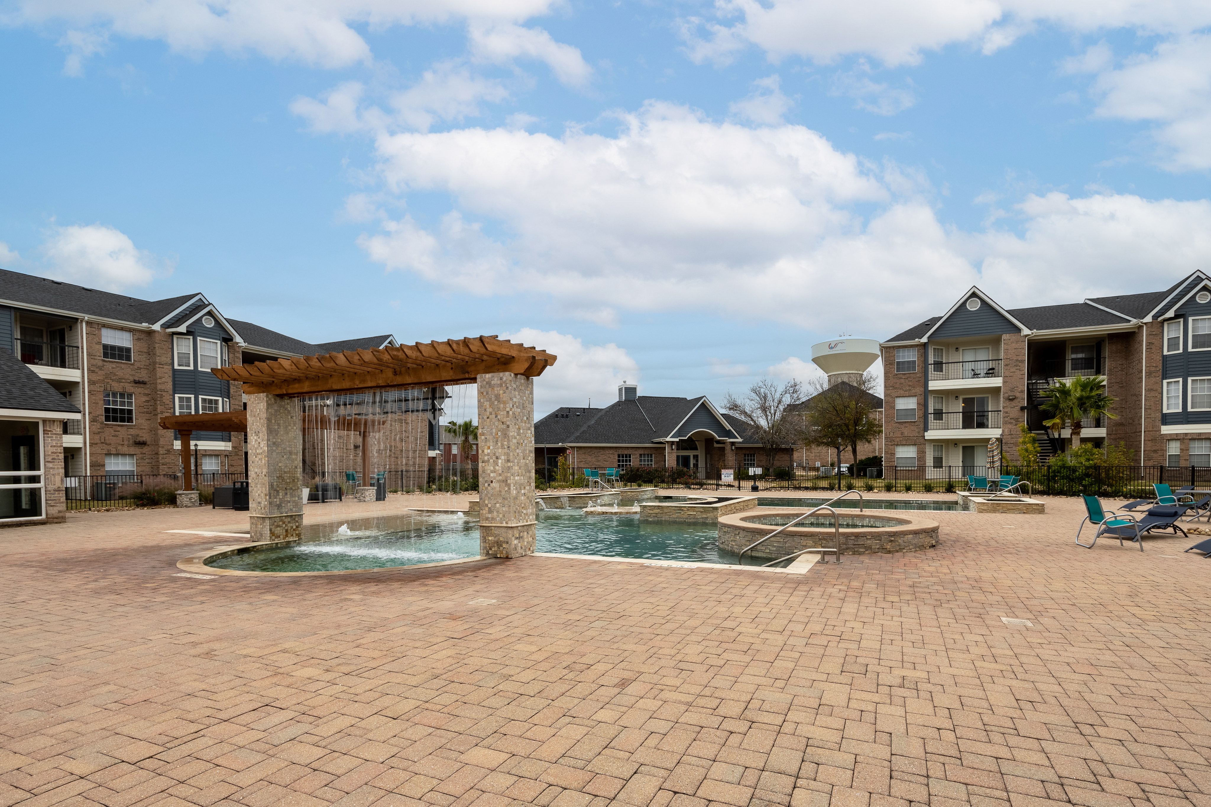 Beautiful apartment complex featuring a luxurious pool with a stone waterfall and lounging area under a clear blue sky.