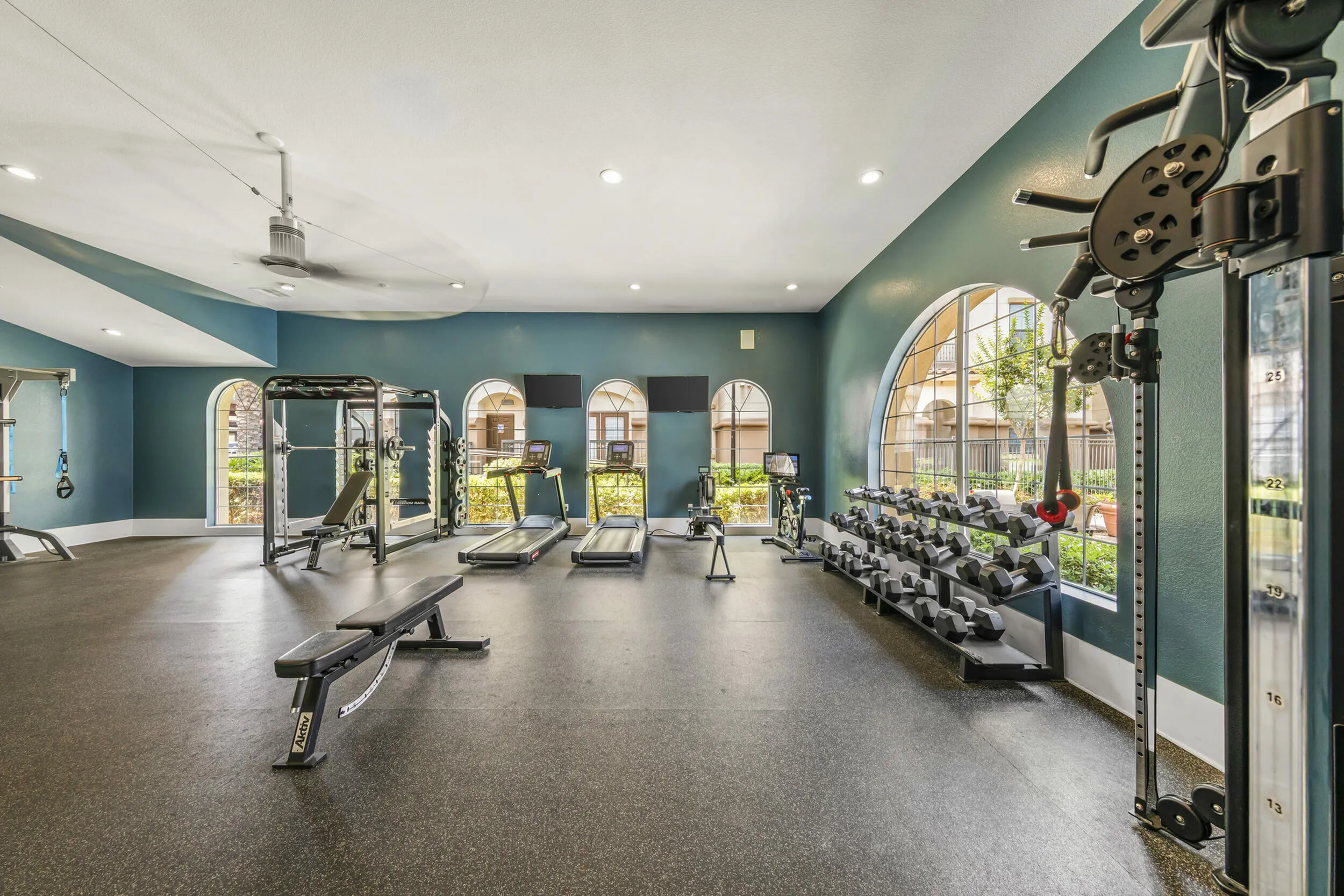 Highlander at North Campus 24/7 fitness center with treadmills, weight benches, and weight rack behind large arched windows in Riverside CA