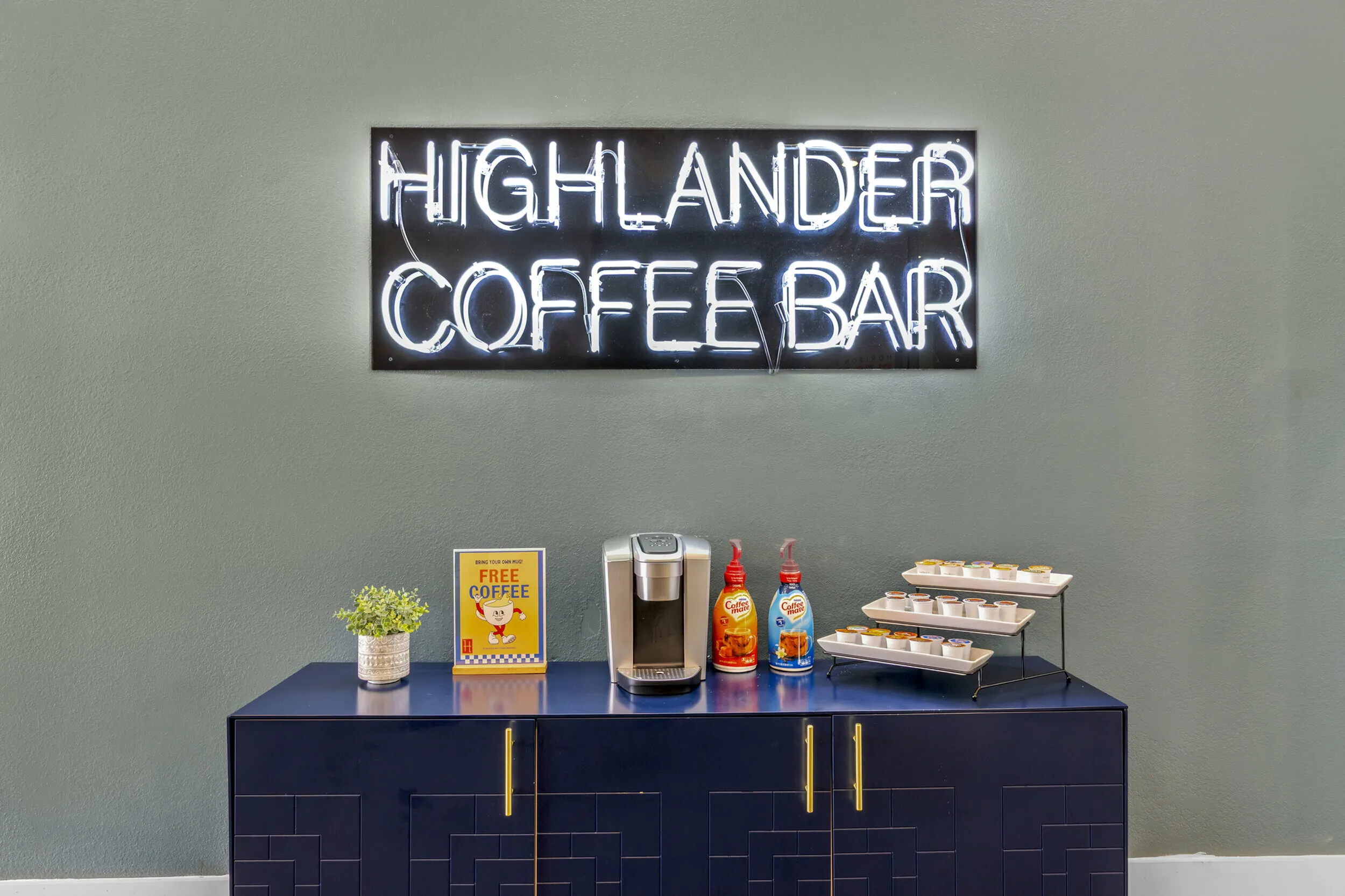 Highlander at North Campus coffee bar with glowing neon sign, espresso machine, and complimentary coffee pods for residents in Riverside CA