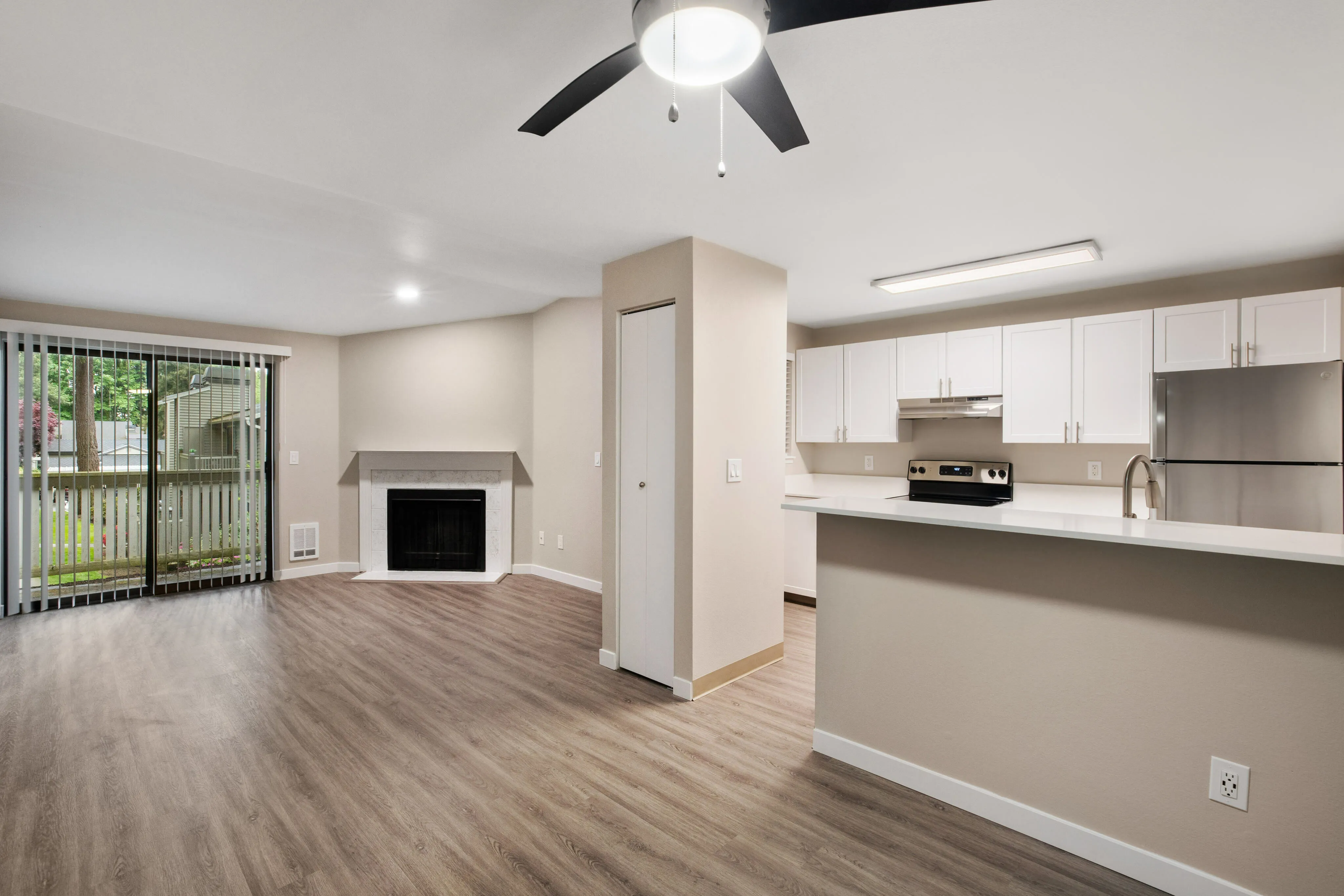 Bright open-concept living area featuring sleek hardwood floors, modern kitchen with stainless steel appliances, and a cozy fireplace, leading to a private outdoor view.