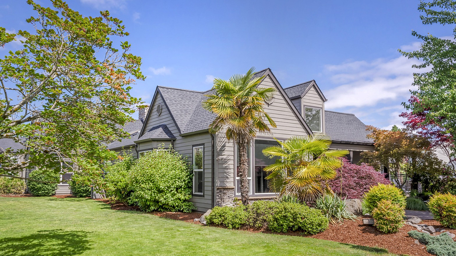 Charming suburban home surrounded by lush greenery and vibrant landscaping under a clear blue sky.