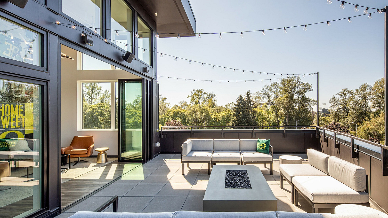 Contemporary outdoor terrace with stylish seating area, fire pit, and string lights overlooking lush greenery.