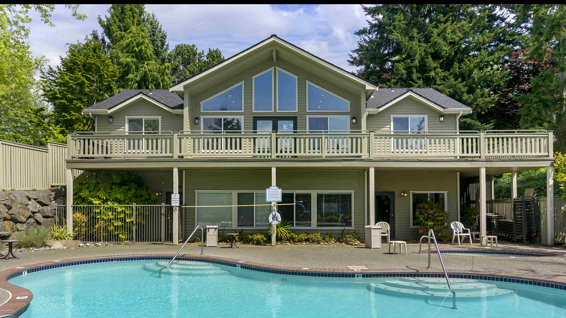 Elegant two-story home with large windows and a stunning backyard swimming pool surrounded by nature.