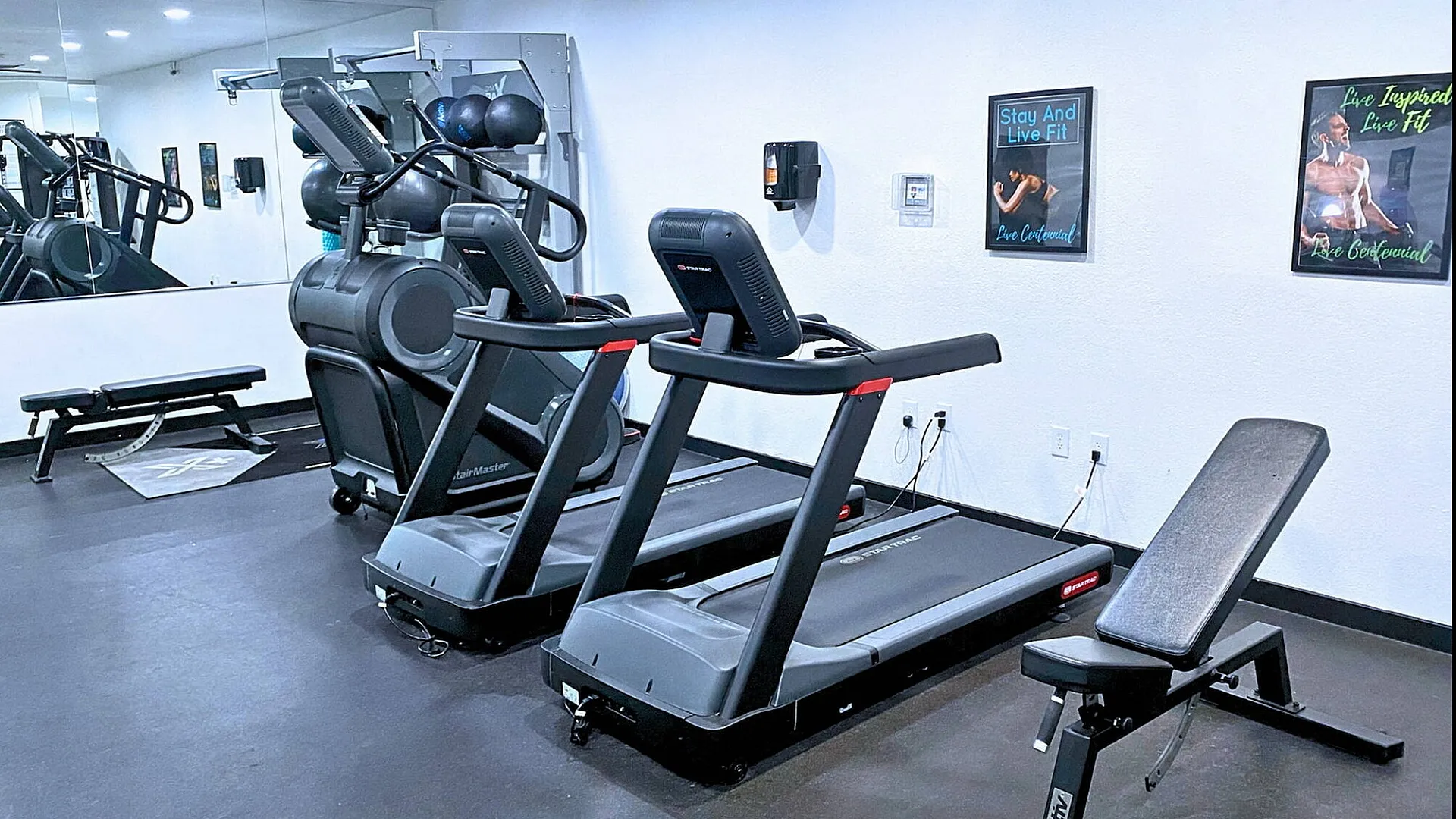 Contemporary gym space equipped with treadmills, workout bench, and motivational posters.