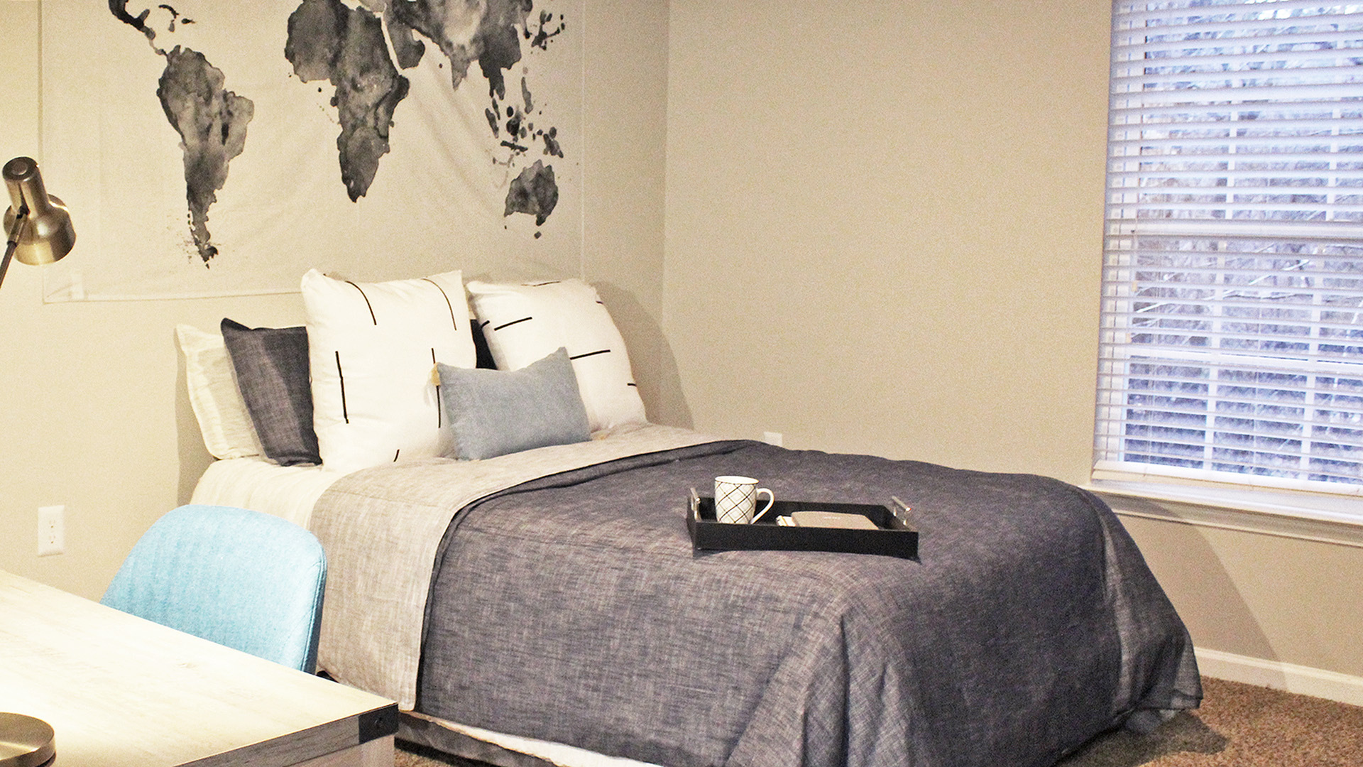 Inviting bedroom with a plush bed, world map wall art, and a large window providing natural light.