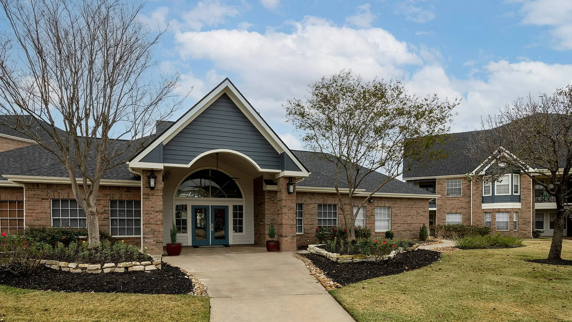 Inviting brick clubhouse building with welcoming entrance and landscaping at The Enclave student apartments in College Station, TX near Texas A&M University