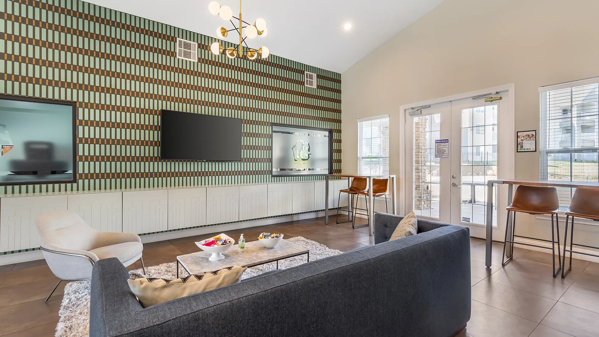Stylish and contemporary lounge with modern decor, featuring a sleek chandelier, a television, and cozy seating.