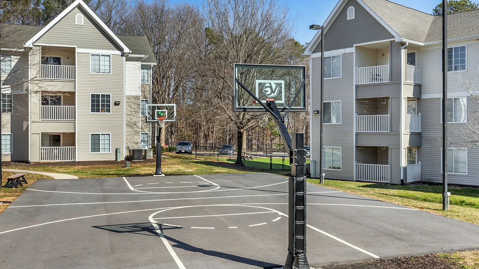 Spacious apartment complex featuring a full-sized basketball court, surrounded by greenery and trees.