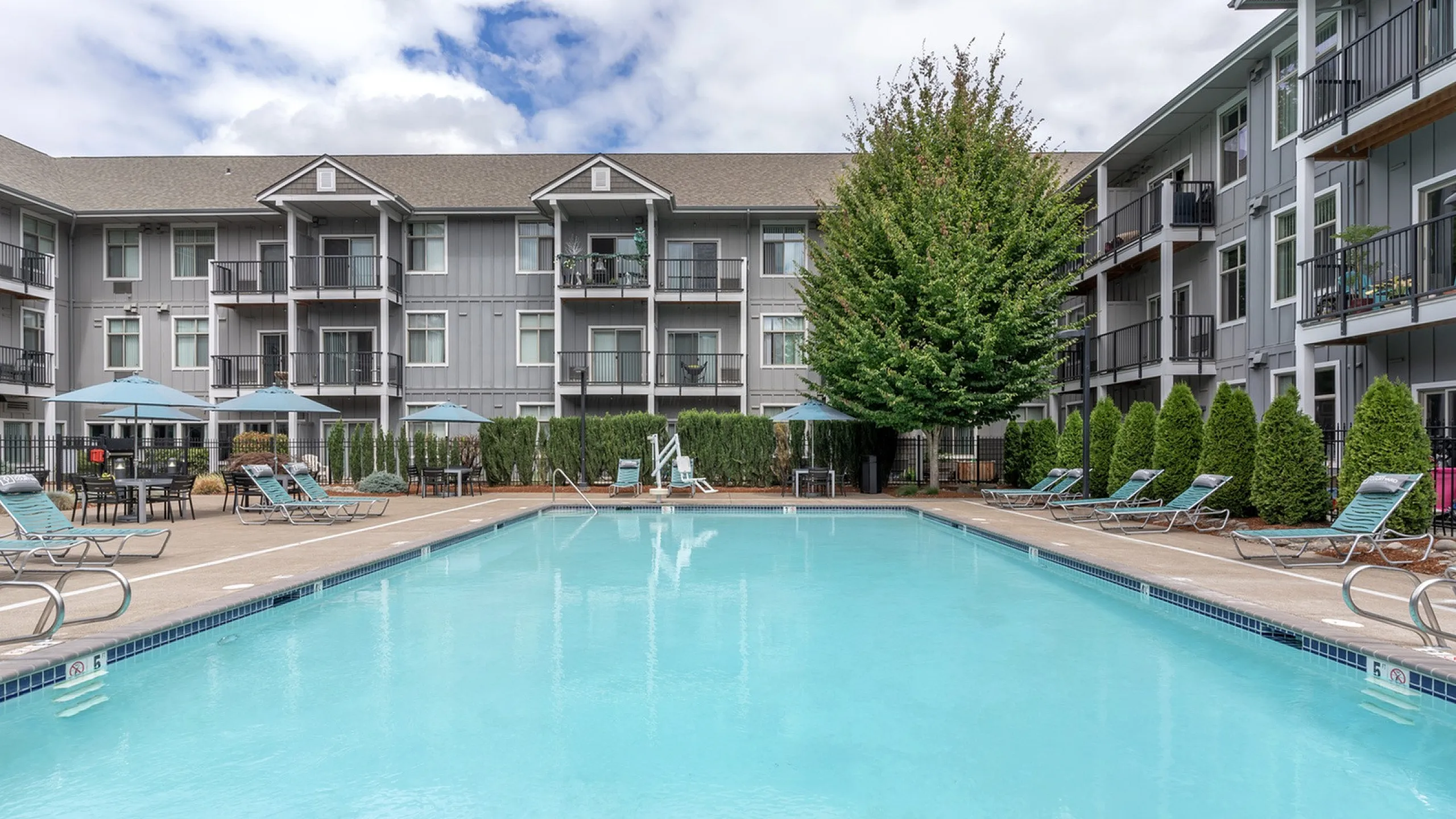 Inviting apartment complex with a pristine swimming pool surrounded by lounge chairs and landscaped greenery.