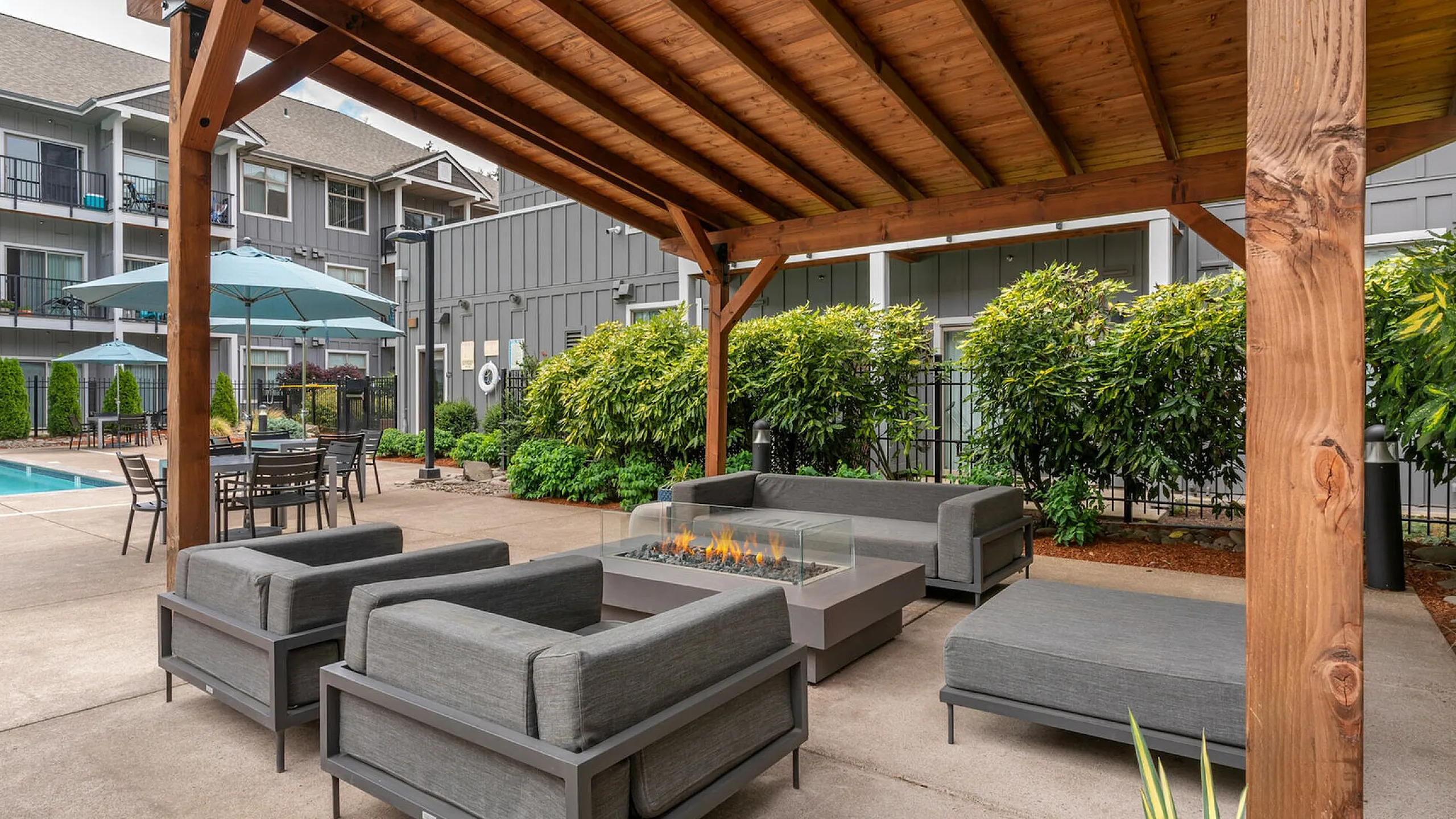 Inviting outdoor lounge with modern seating, a fire pit, and poolside umbrellas under a wooden pergola.