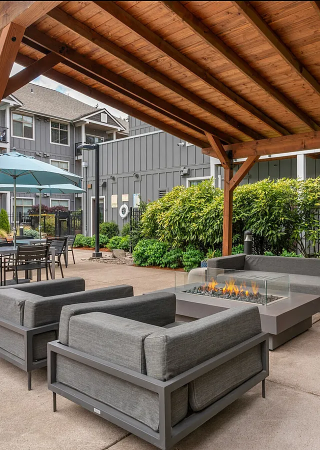Luxurious outdoor lounge area with plush seating and modern fire pit under a wooden pergola, perfect for relaxation near the sparkling poolside.