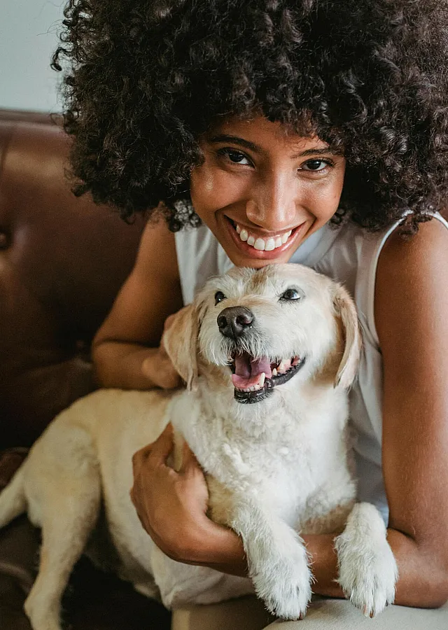 Joyful woman with curly hair embracing a happy dog on a luxurious leather sofa.