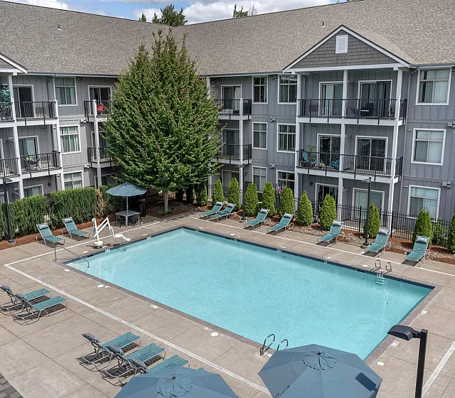Elegant apartment complex featuring a sparkling outdoor swimming pool surrounded by modern lounge chairs and shaded seating areas.