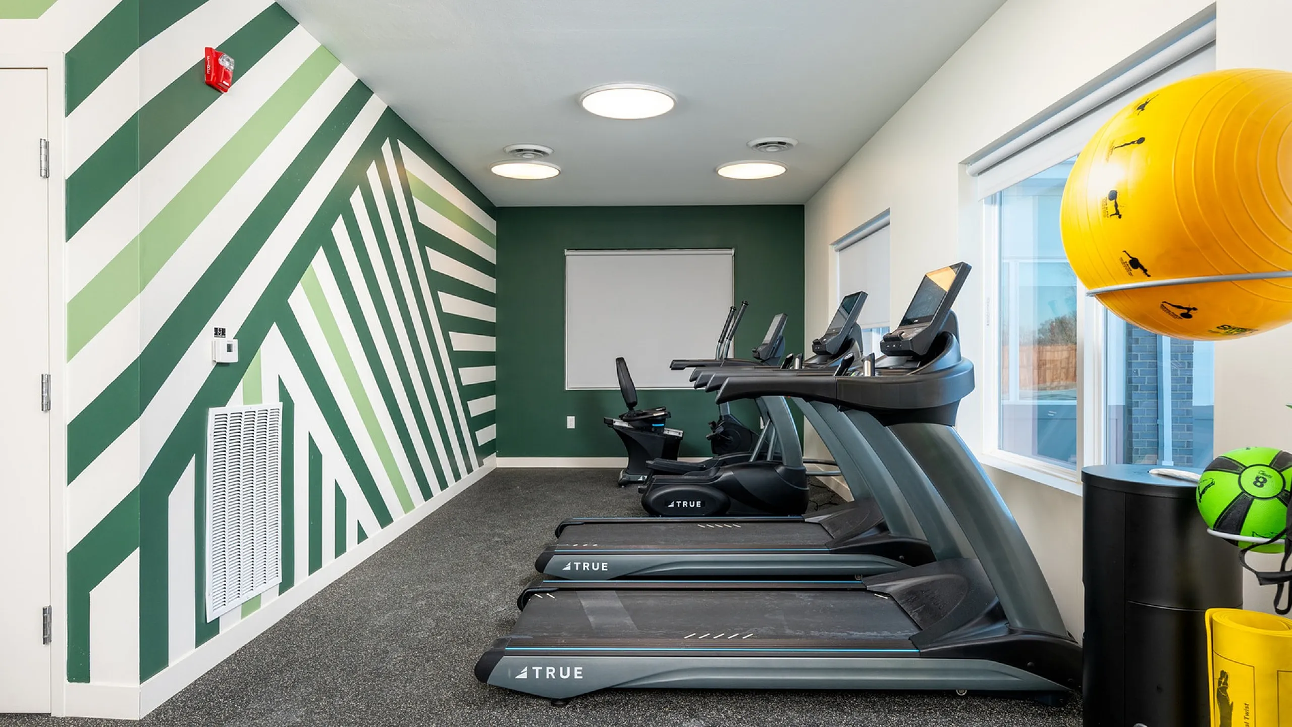 Modern fitness room featuring sleek treadmills, stylish geometric wall design, and abundant natural light.
