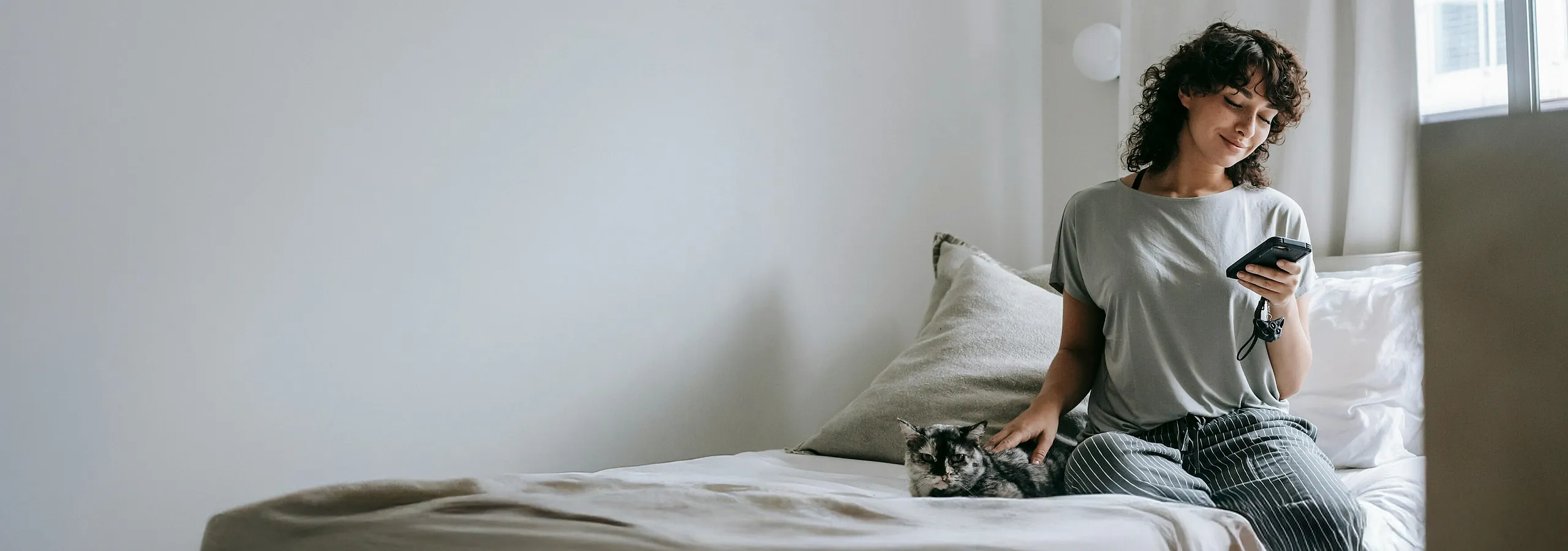 Cozy bedroom setting with natural light, featuring a person enjoying a peaceful moment with a cat, highlighting comfort and relaxation.