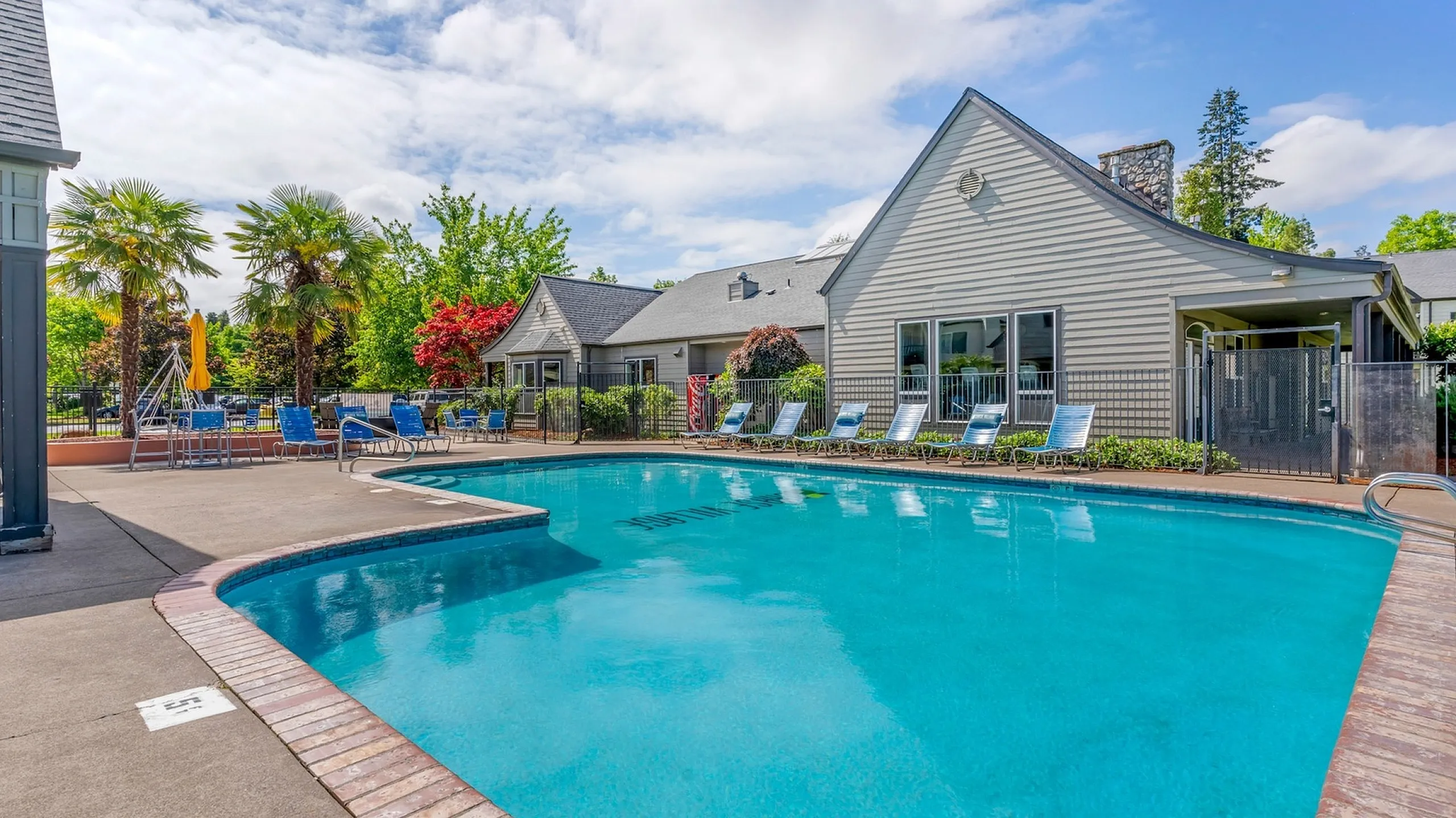 Inviting outdoor swimming pool with adjacent lounge chairs, surrounded by lush greenery and a charming residential building.