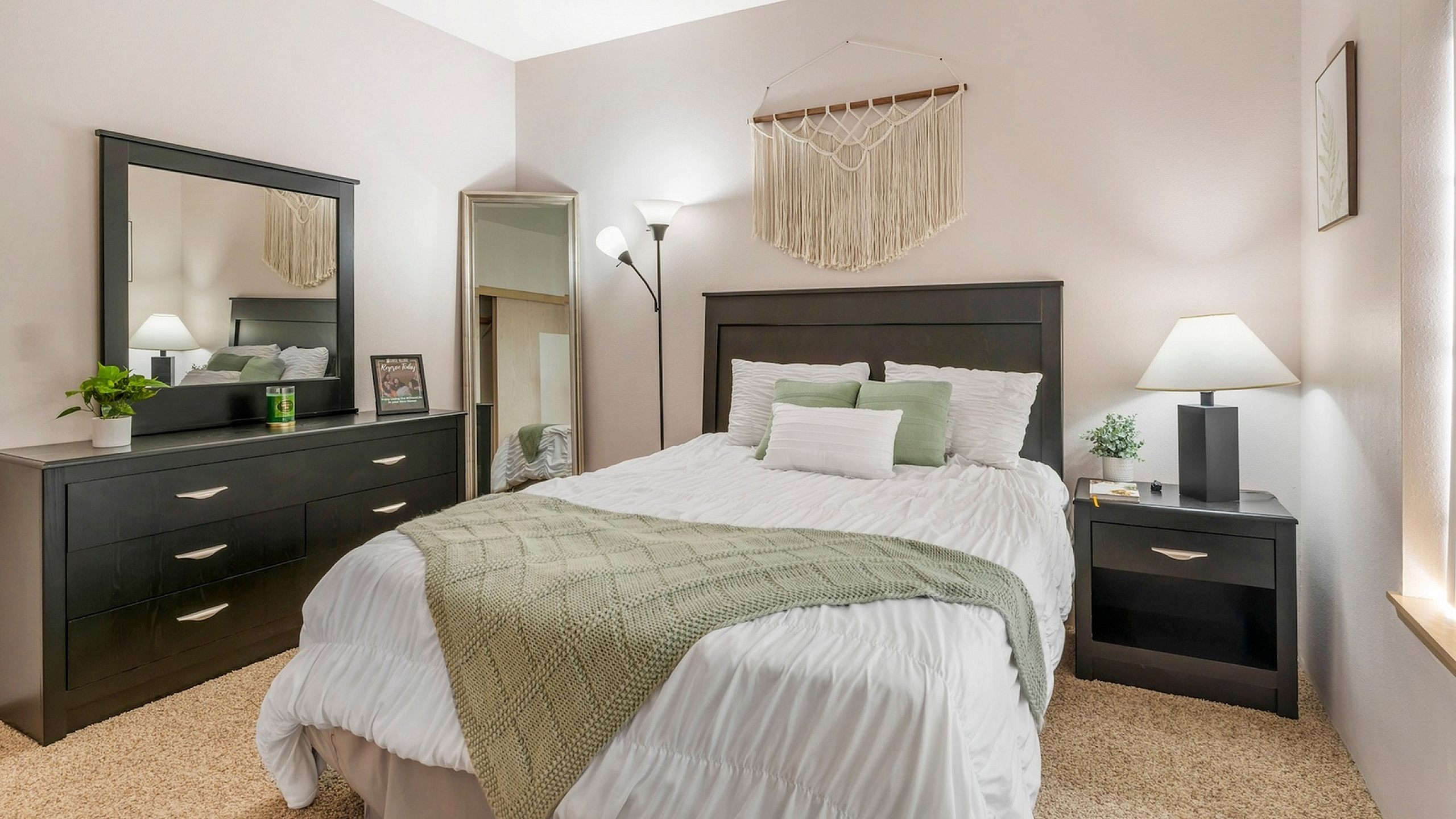 Elegant bedroom with cozy decor, featuring a modern black dresser, comfortable bed with plush pillows and soft blanket, accented by natural lighting and stylish wall art.