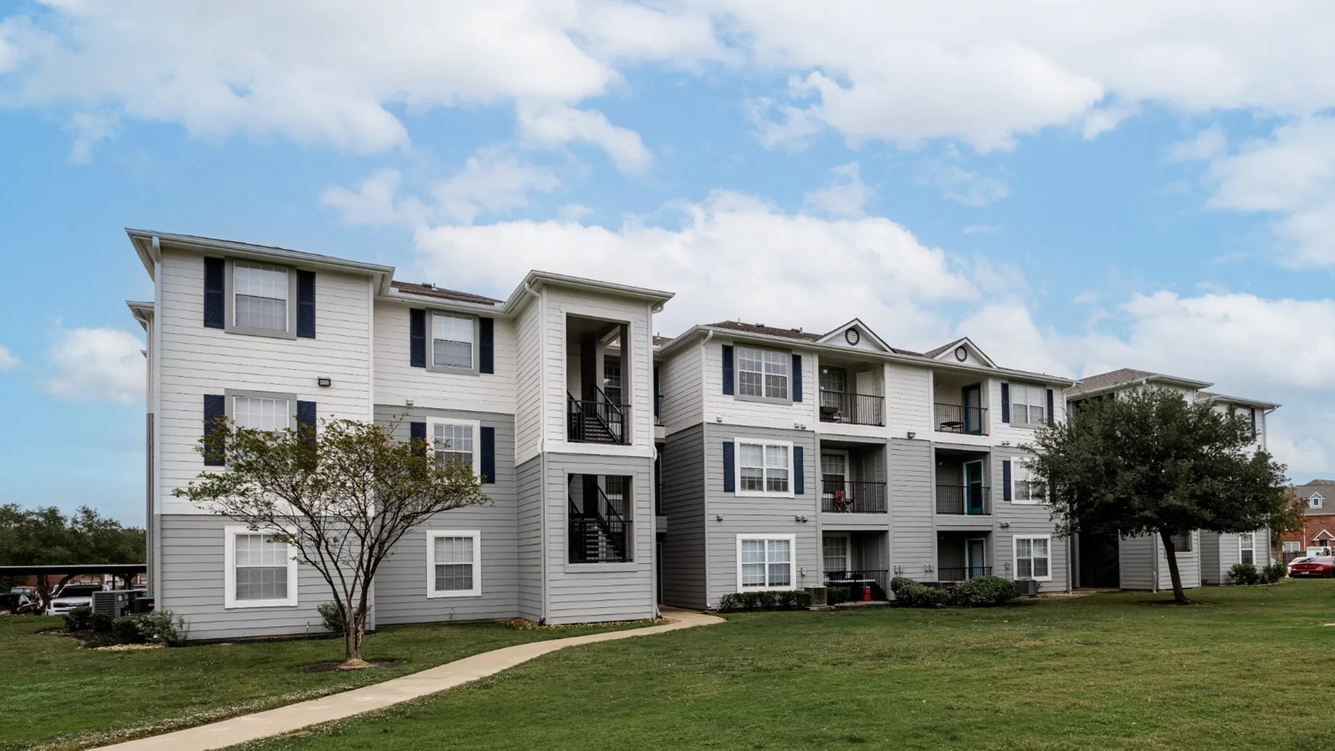 Charming apartment complex with modern architecture and lush green surroundings under a bright blue sky.